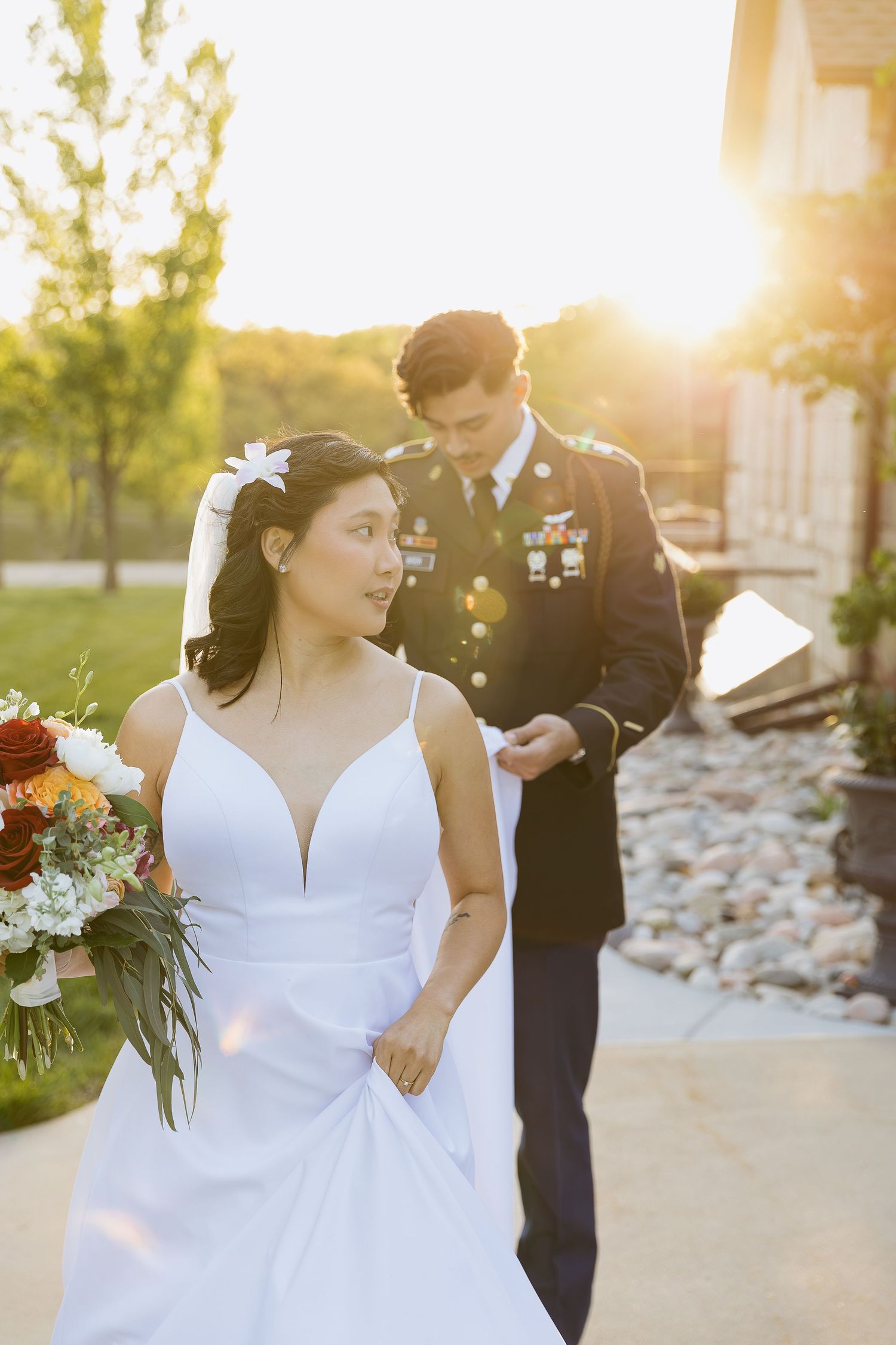 Military servicemember and bride in white dress share a sunset moment during outdoor wedding ceremony.