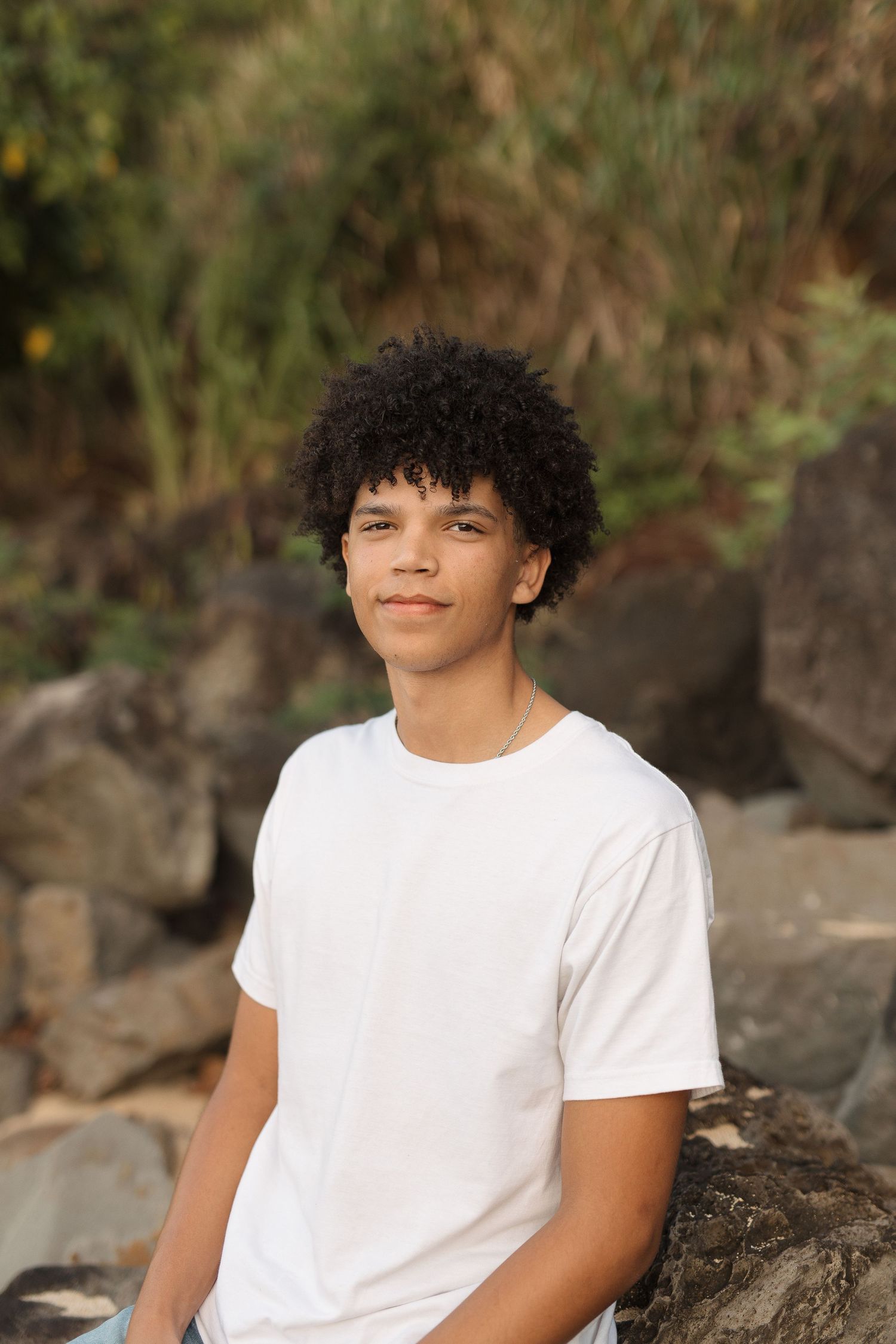 Natural outdoor portrait of a young person in white t-shirt against rocky beach at sunset waimea bay senior session north shore oahu ha