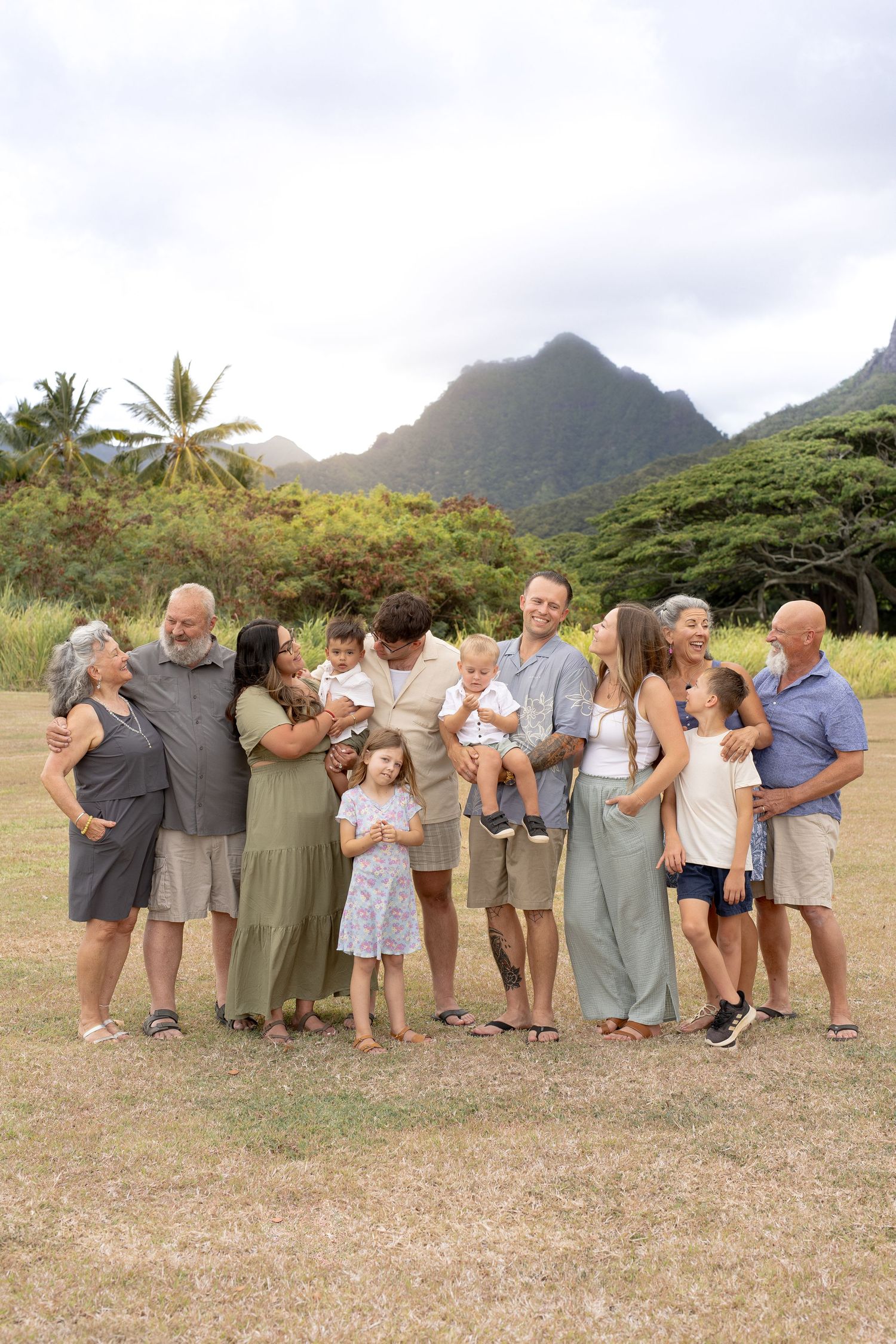 Large group of people hugging in a line on grassy field with dramatic mountains and palm trees in background.