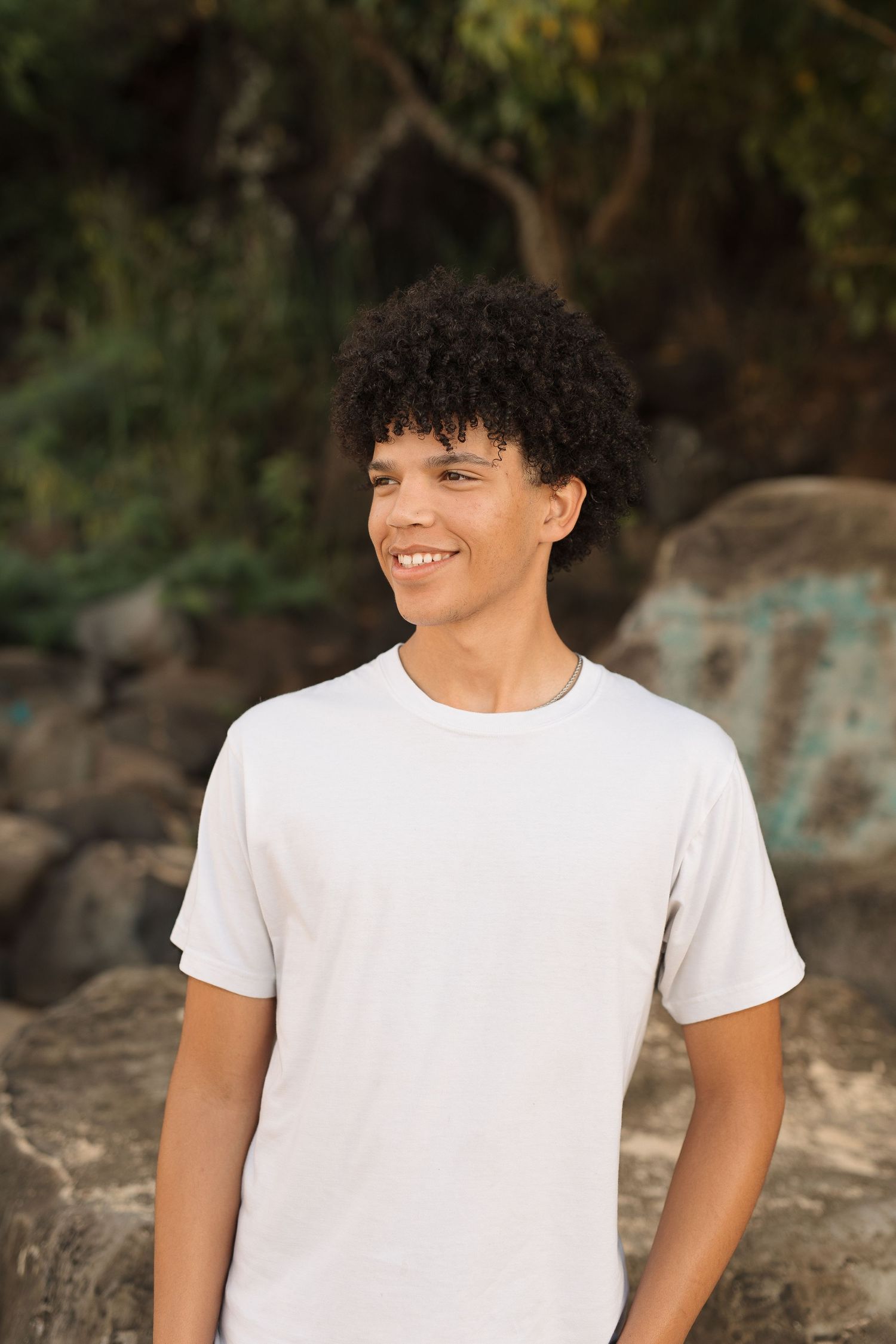 Portrait of person in white t-shirt smiling against rocky beach backdrop.   waimea bay senior session north shore oahu hawaii
