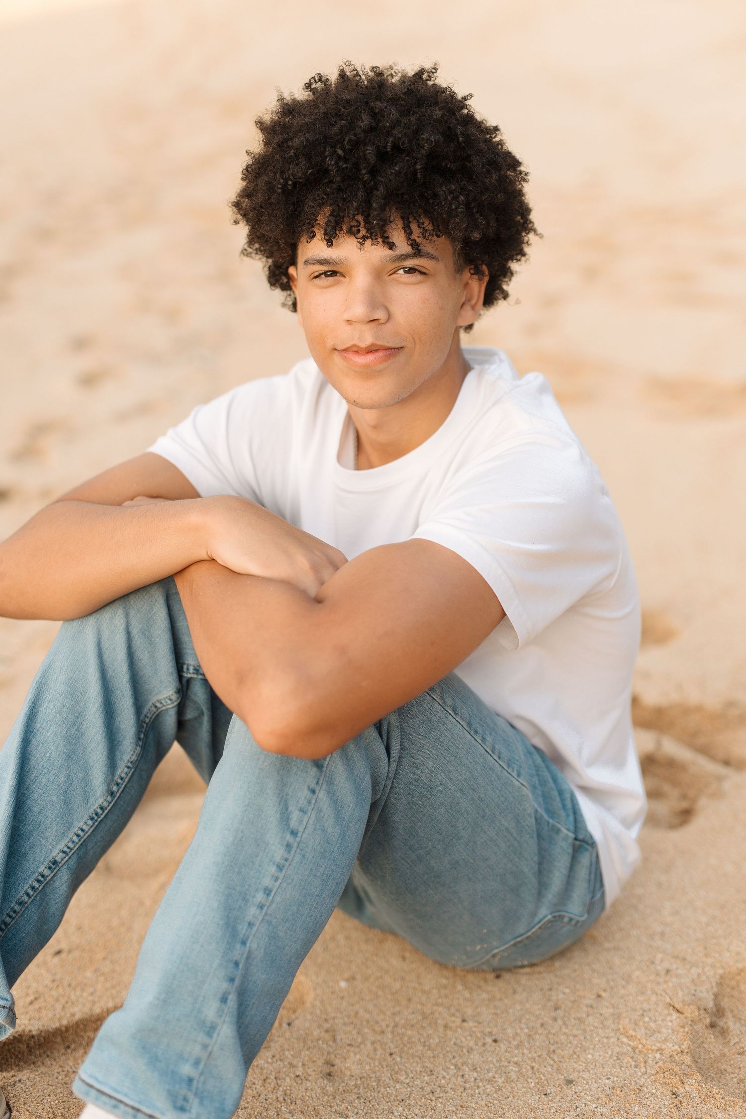 Casual beach portrait of person in white t-shirt and jeans sitting on sand.waimea bay senior session north shore oahu hawaii