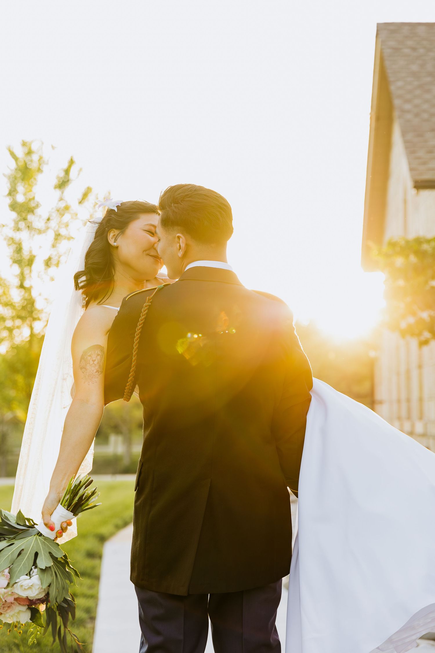 Newlyweds share a romantic kiss at sunset with sunflare behind them.