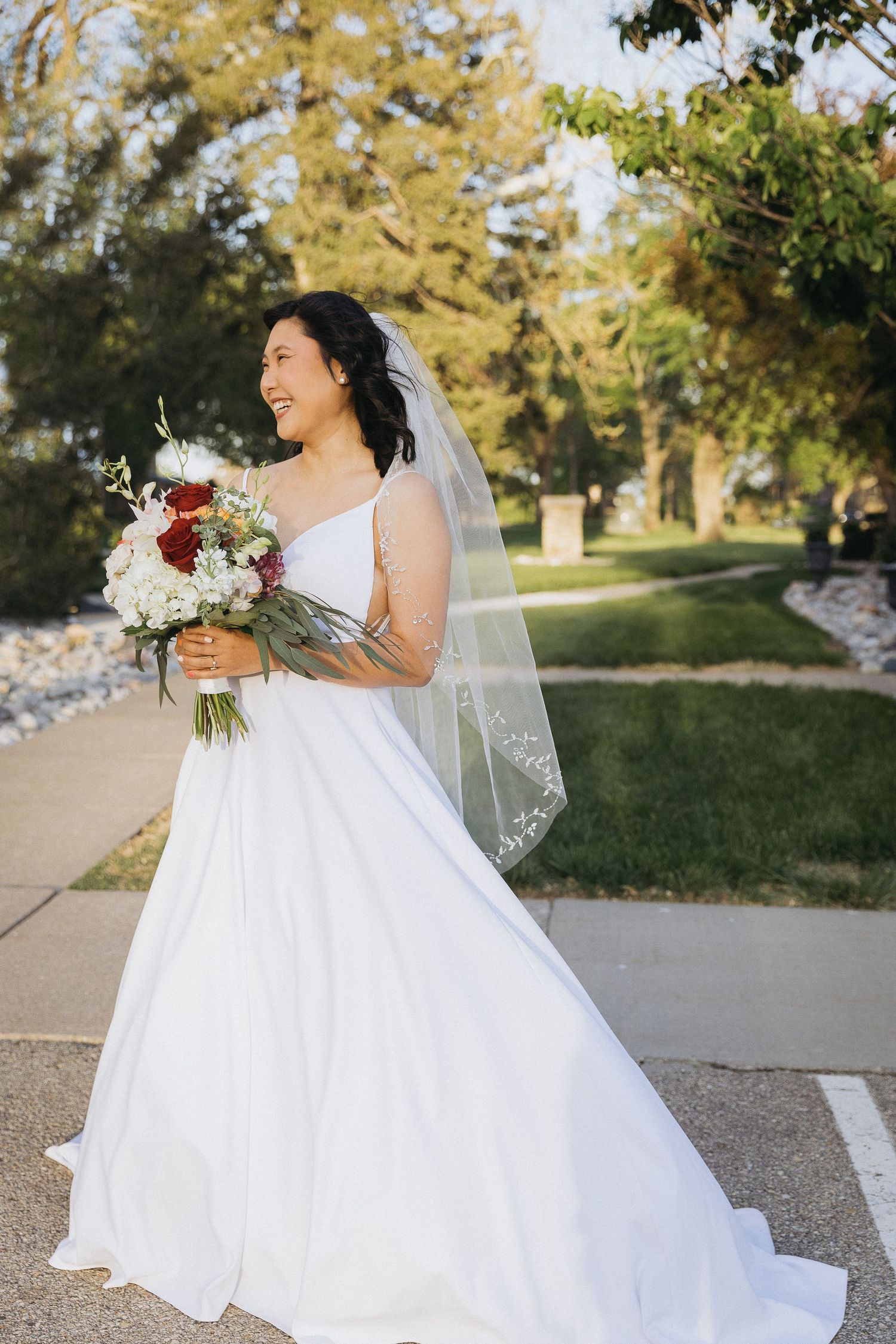 A bride in a white gown holds a colorful bouquet while standing on a garden pathway.