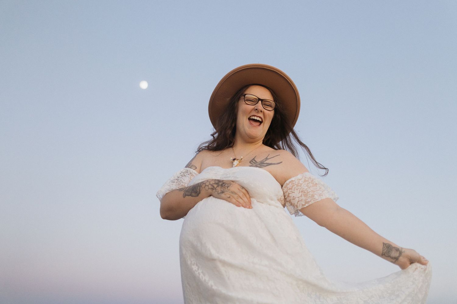 Joyful maternity portrait with moon visible in dusky sky background.