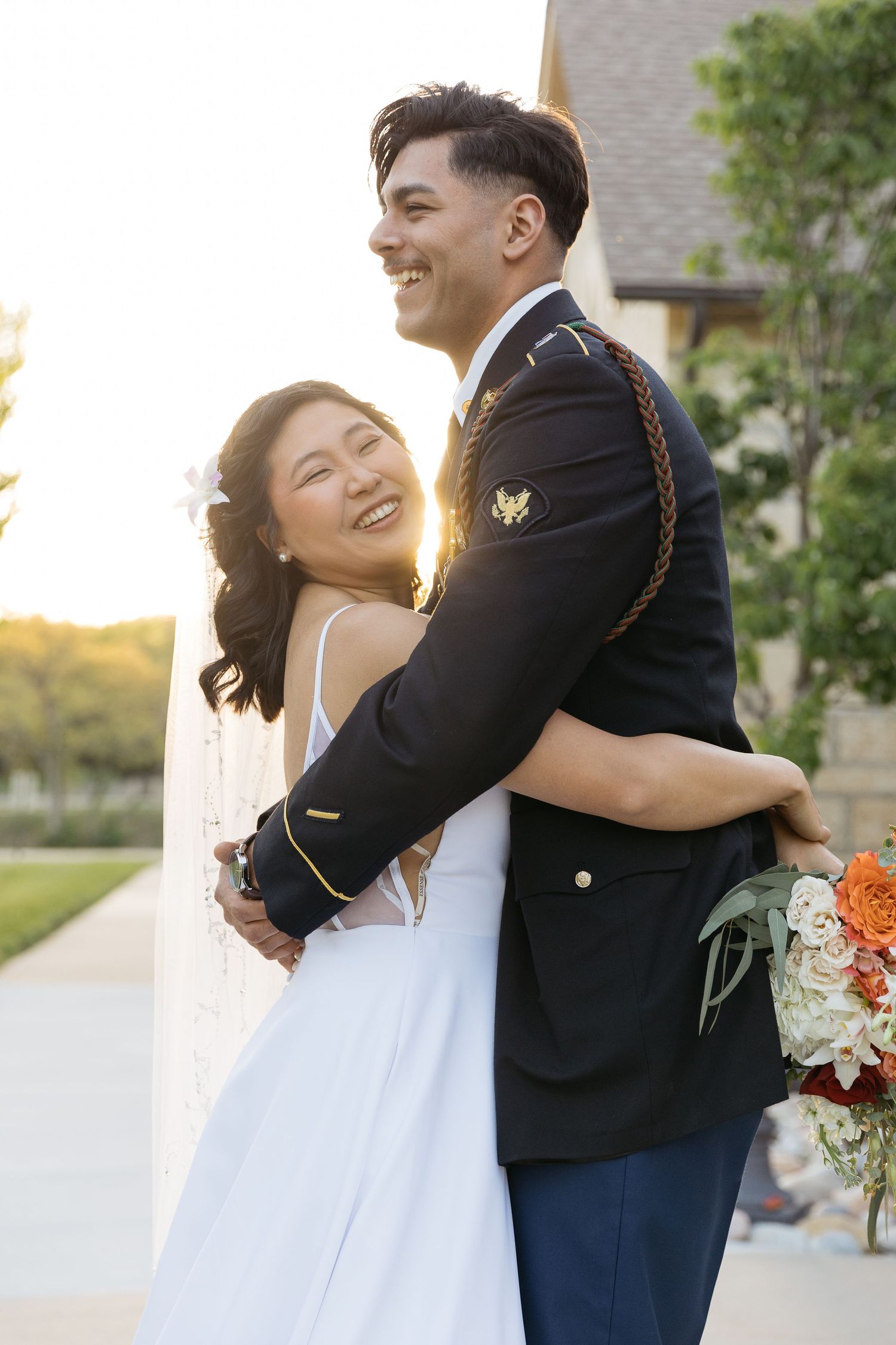 A joyful wedding couple embraces outdoors during golden hour with a beautiful building backdrop.