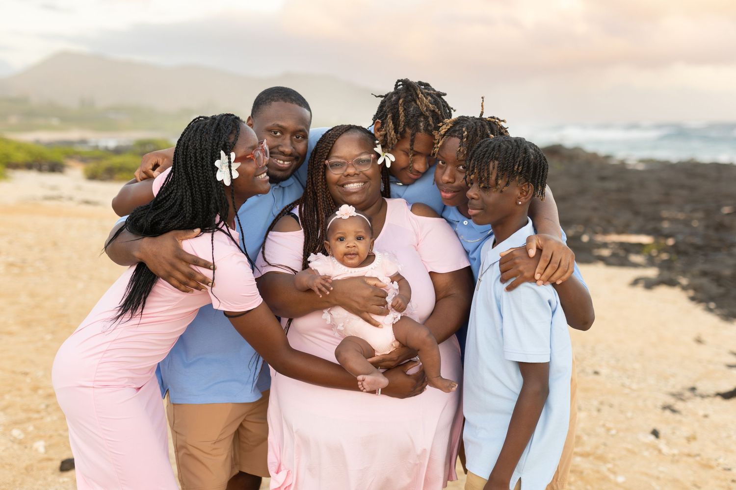 A loving family group hugs together on a scenic beach during sunset.