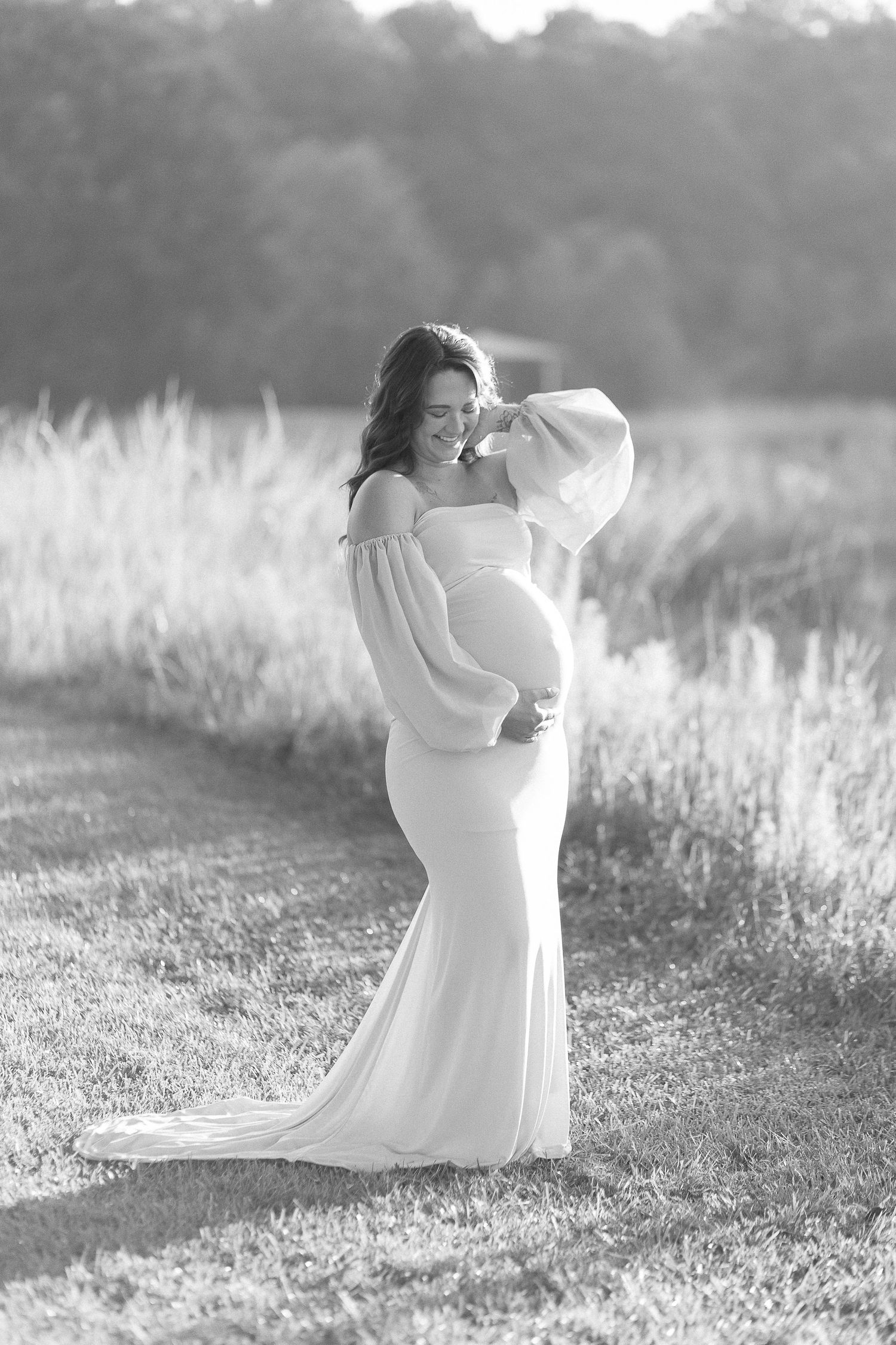 An elegant maternity portrait in black and white showing a woman in a long white gown.
