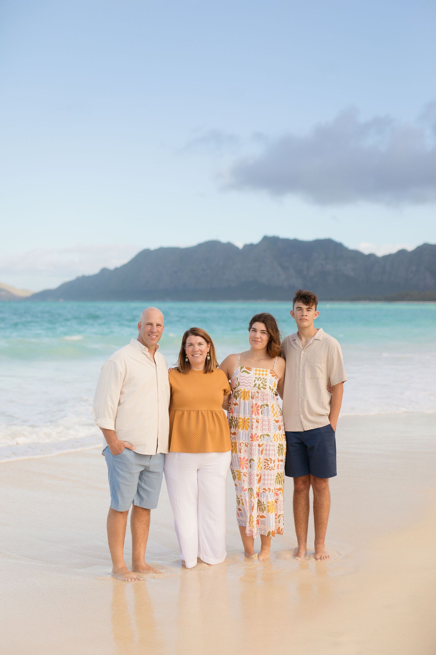 A group of people standing together on a scenic tropical beach with turquoise waters and mountains in the background.