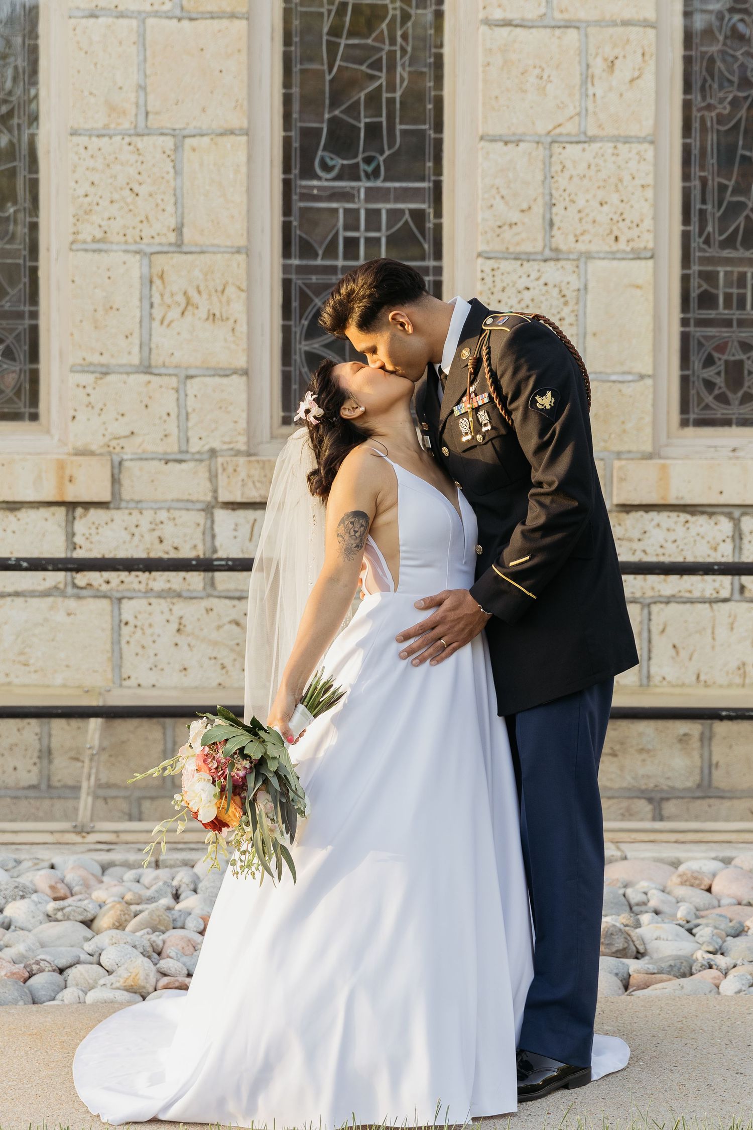 A romantic wedding moment captured in golden sunlight against a stone church wall.
