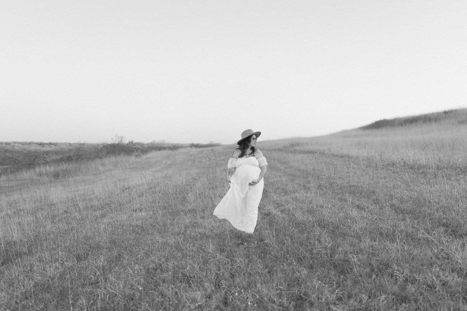 Black and white photo of a person in flowing white dress twirling in an open field.