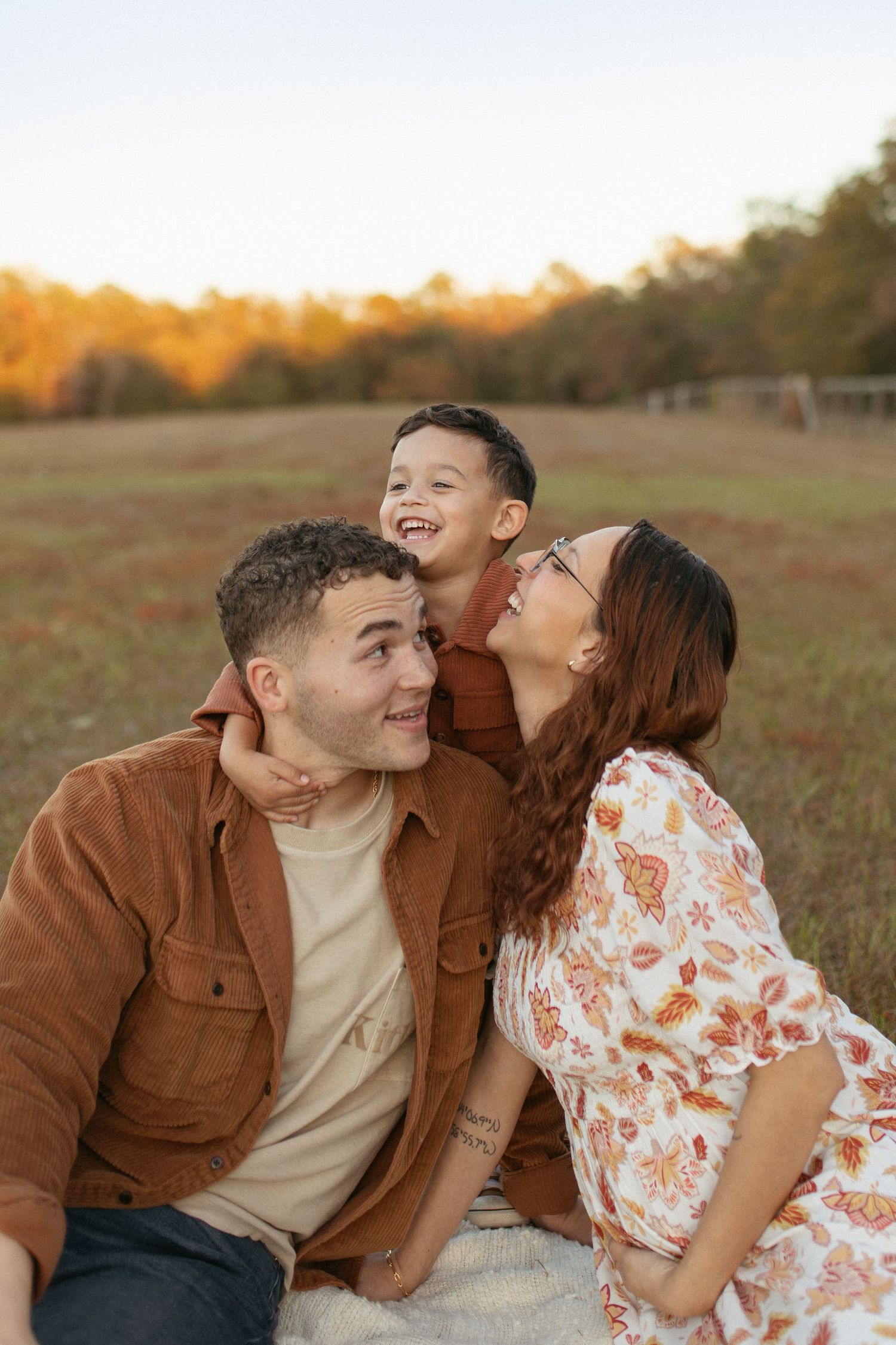 Family laughing together during outdoor photo session in golden sunset light.