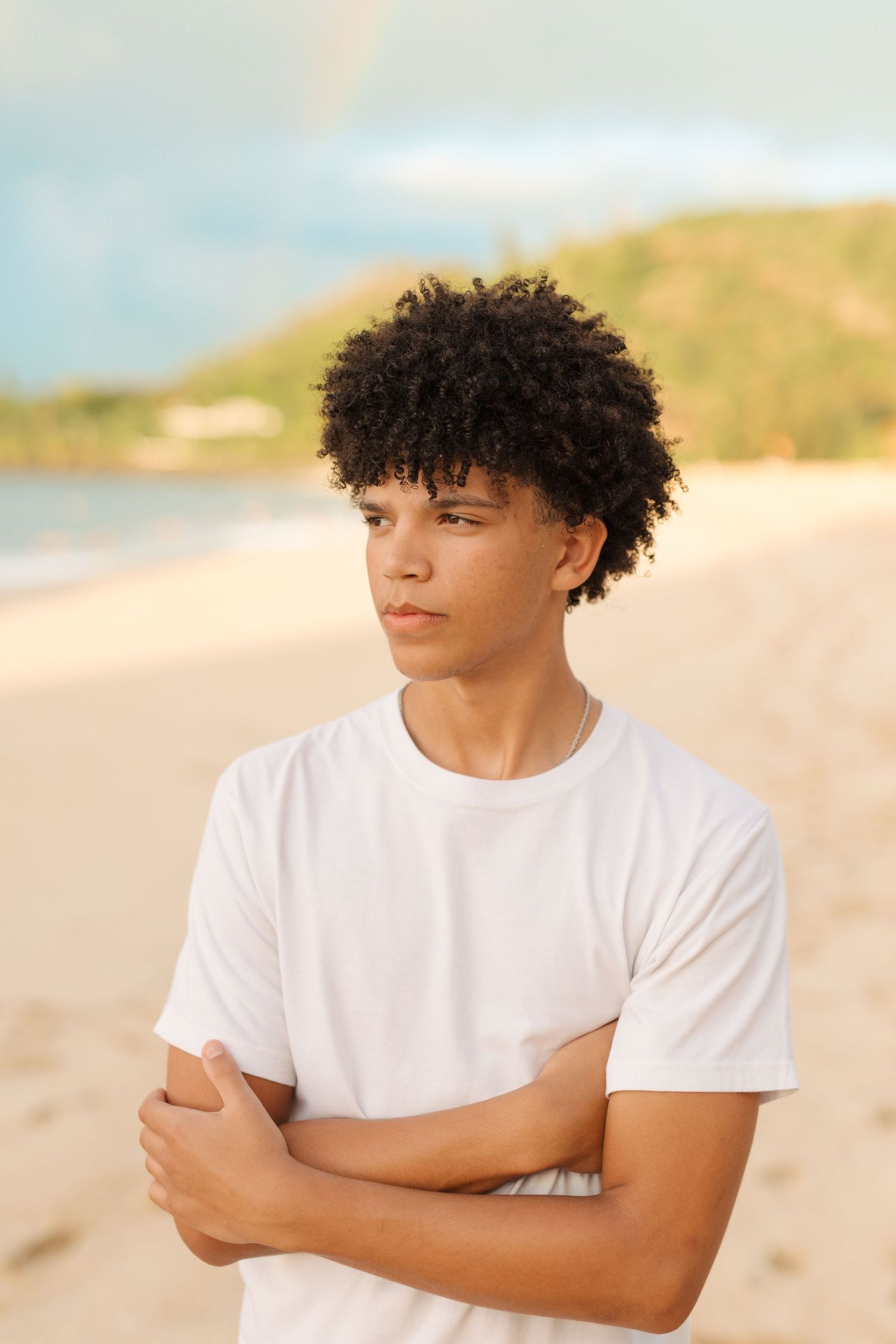 Thoughtful beach portrait at sunset with arms crossed wearing white t-shirt. waimea bay senior session north shore oahu hawaii