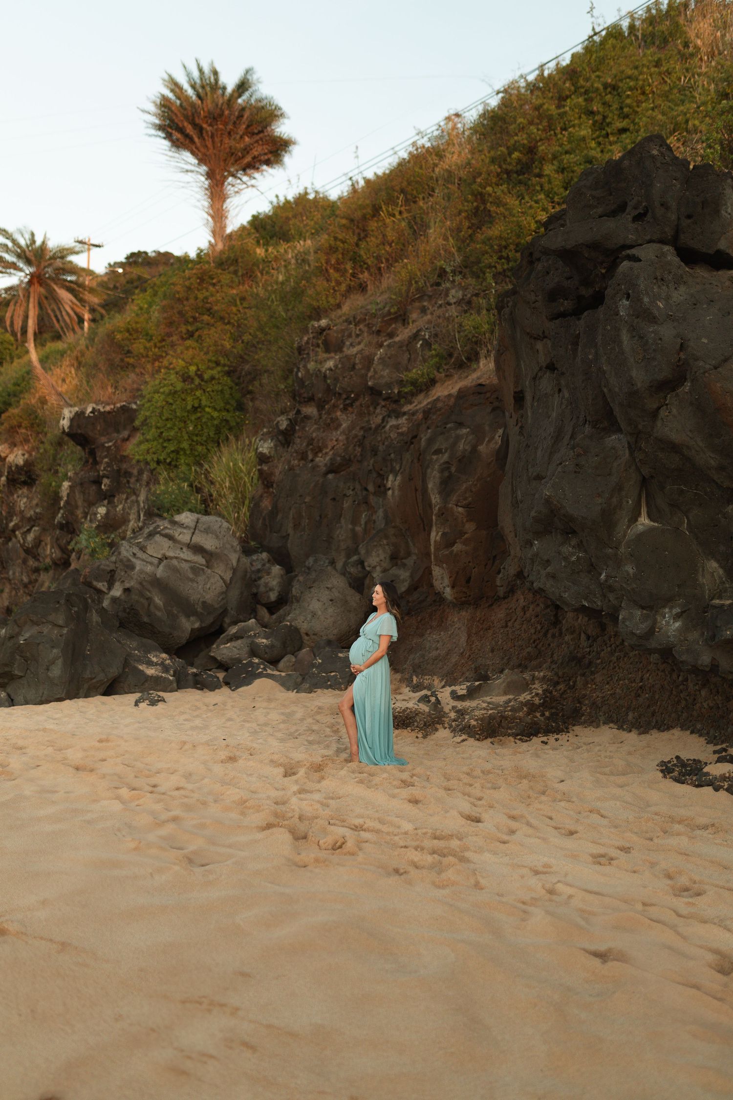 A person in a teal dress poses against dramatic rocky cliffs at sunset.