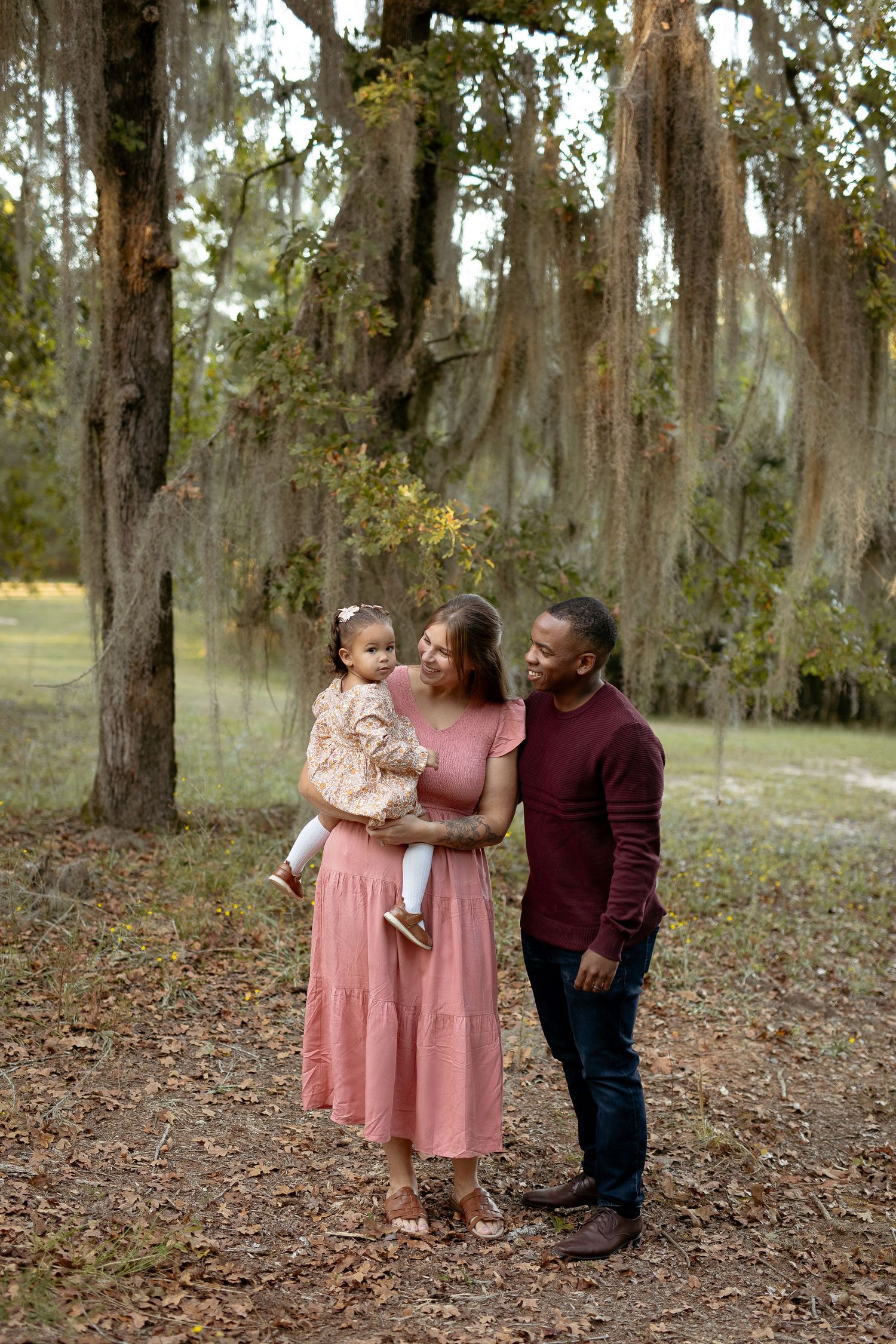 Family enjoying a tender moment together beneath Spanish moss-draped trees in a park setting.