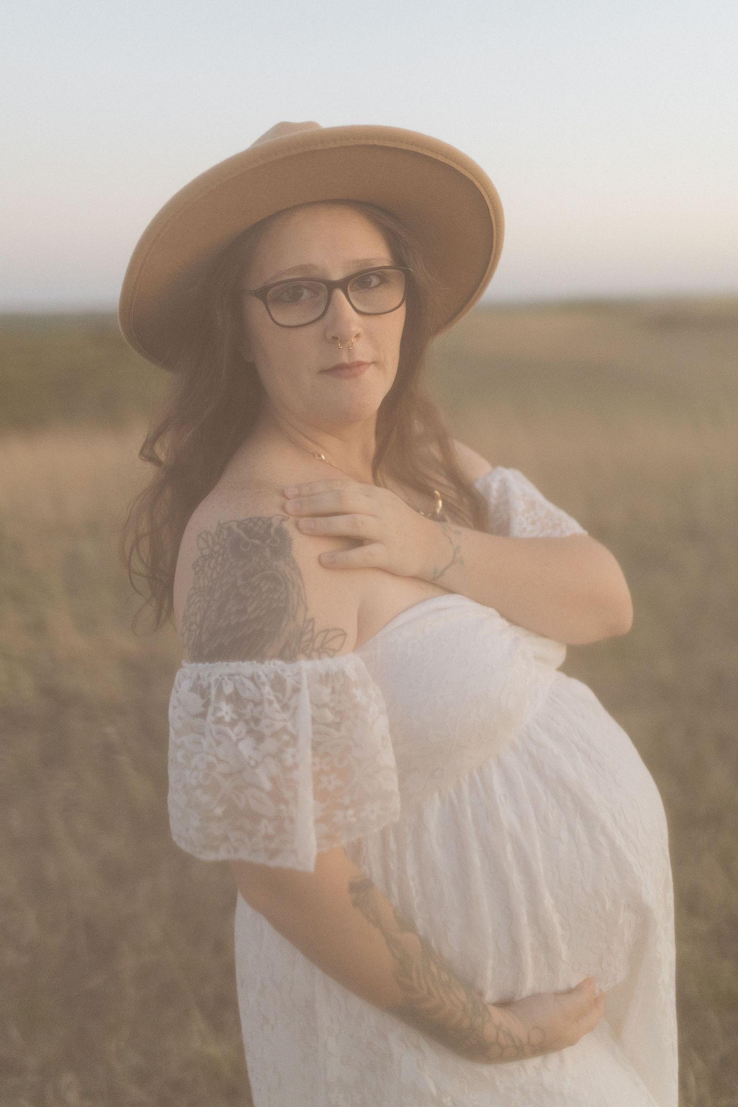 Dreamy sunset maternity portrait in white lace dress and brown hat.