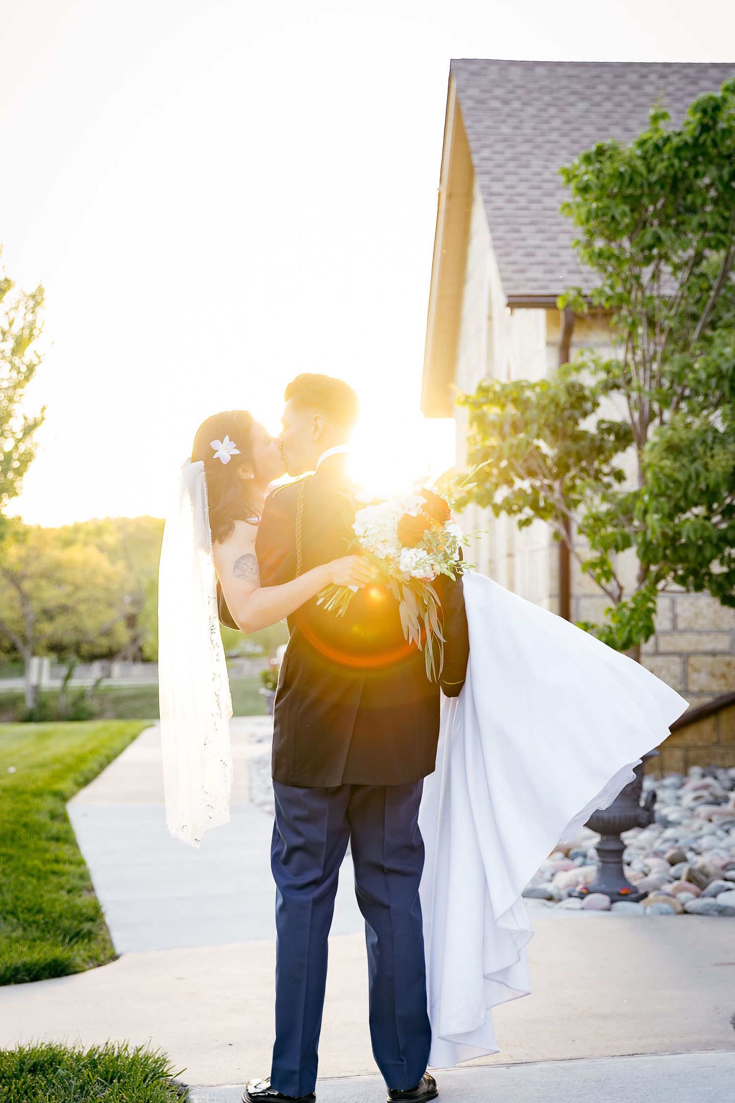 Romantic silhouette of a couple embracing outdoors during golden hour sunset with bride's flowing white dress veil.
