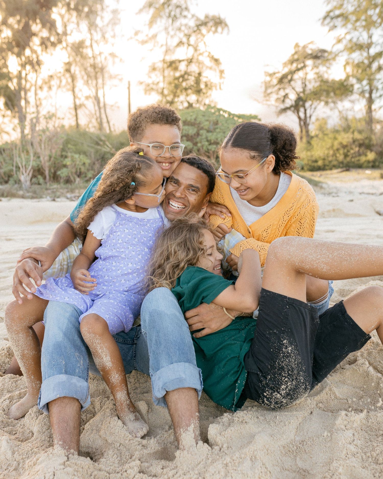 Family enjoying a playful moment together on a sandy beach during golden hour.