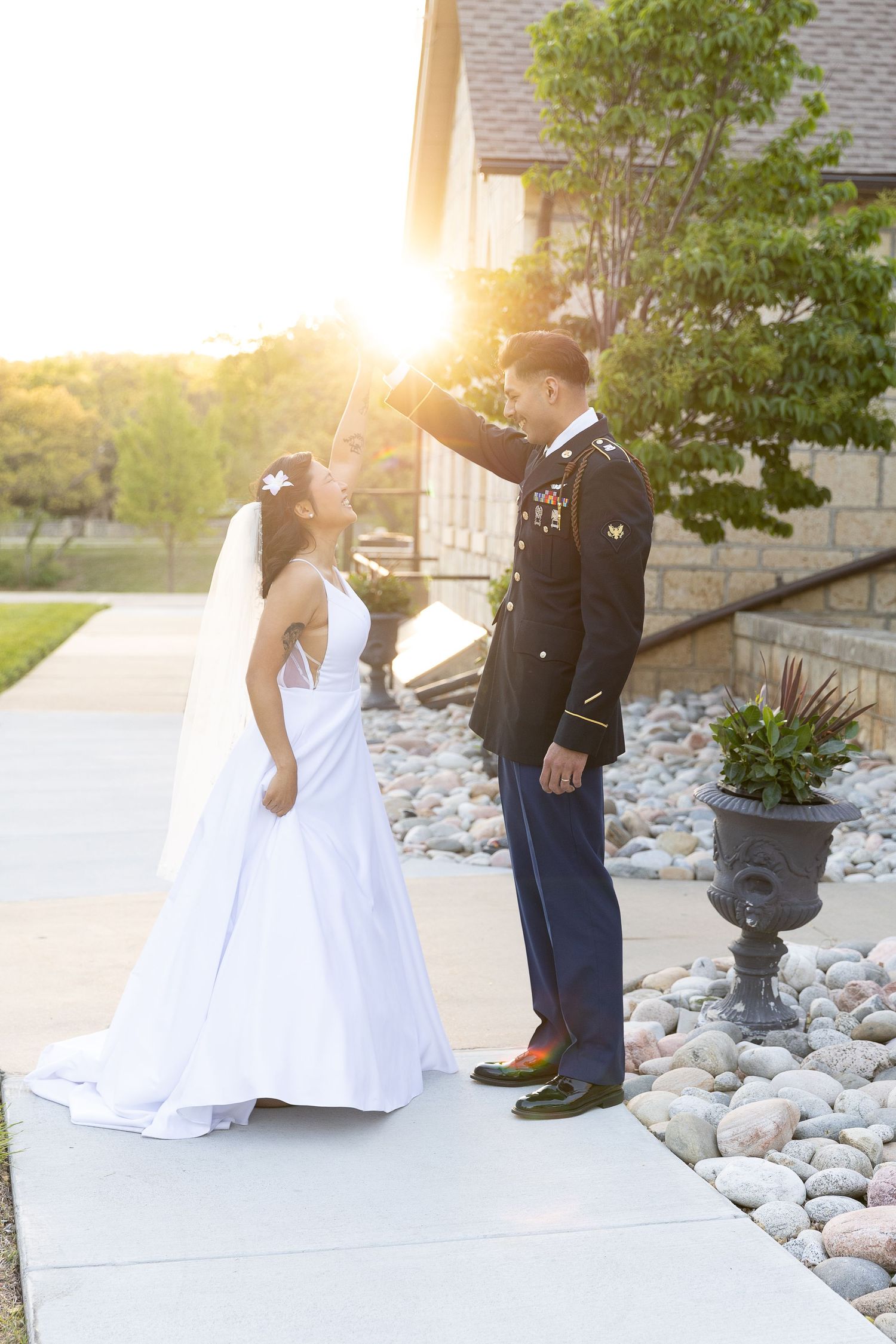 A couple in wedding attire sharing a romantic moment at sunset outside a stone building.