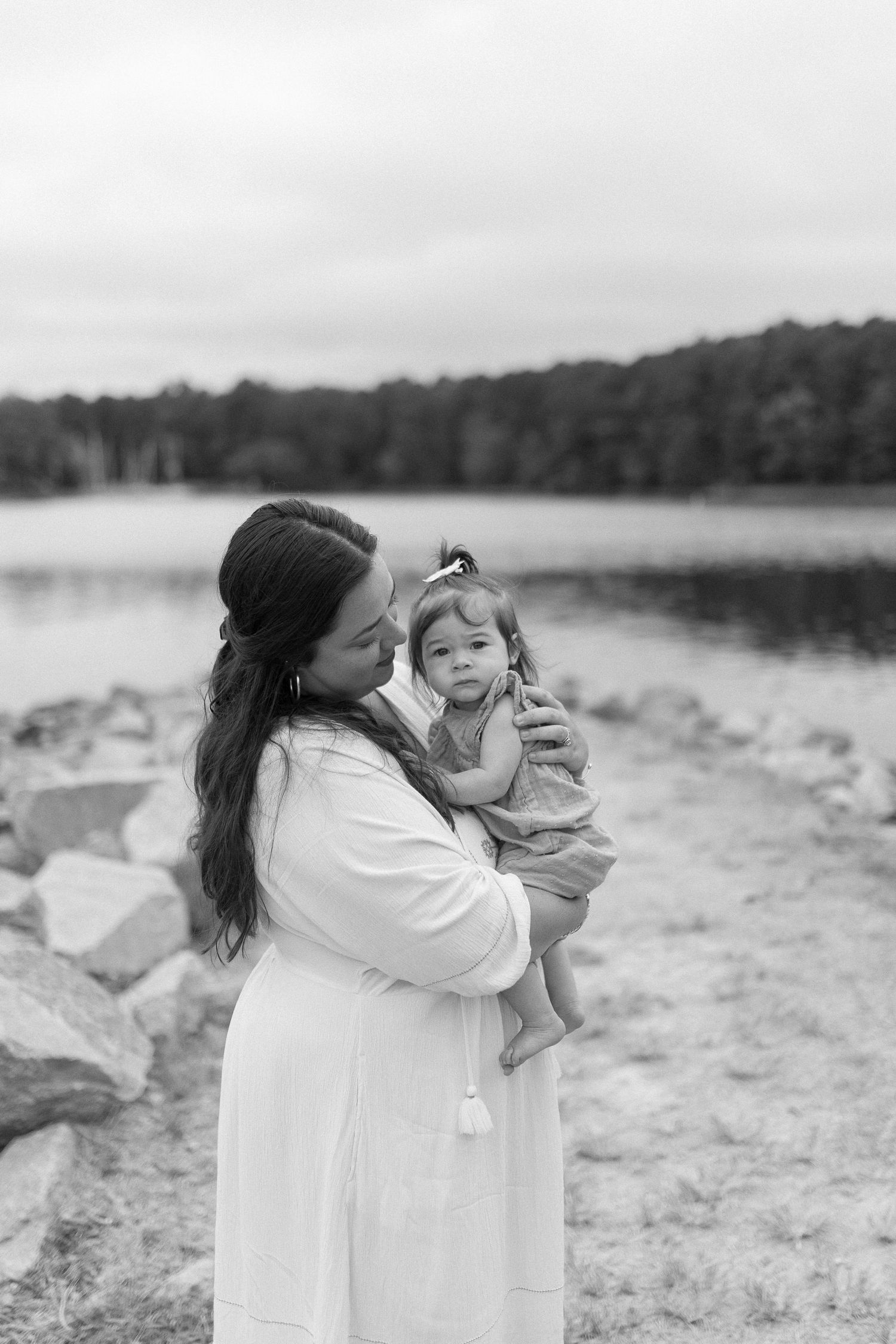 Black and white portrait captured by lakeside with rocky shoreline.