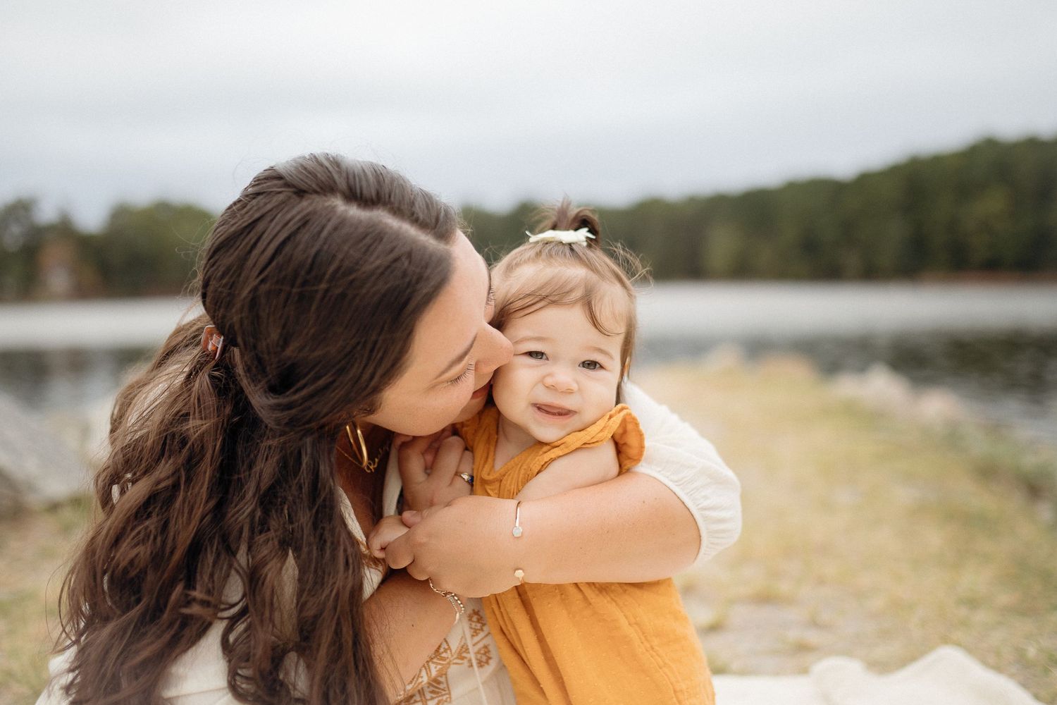 Mother and child embrace while laughing together by a serene lake.