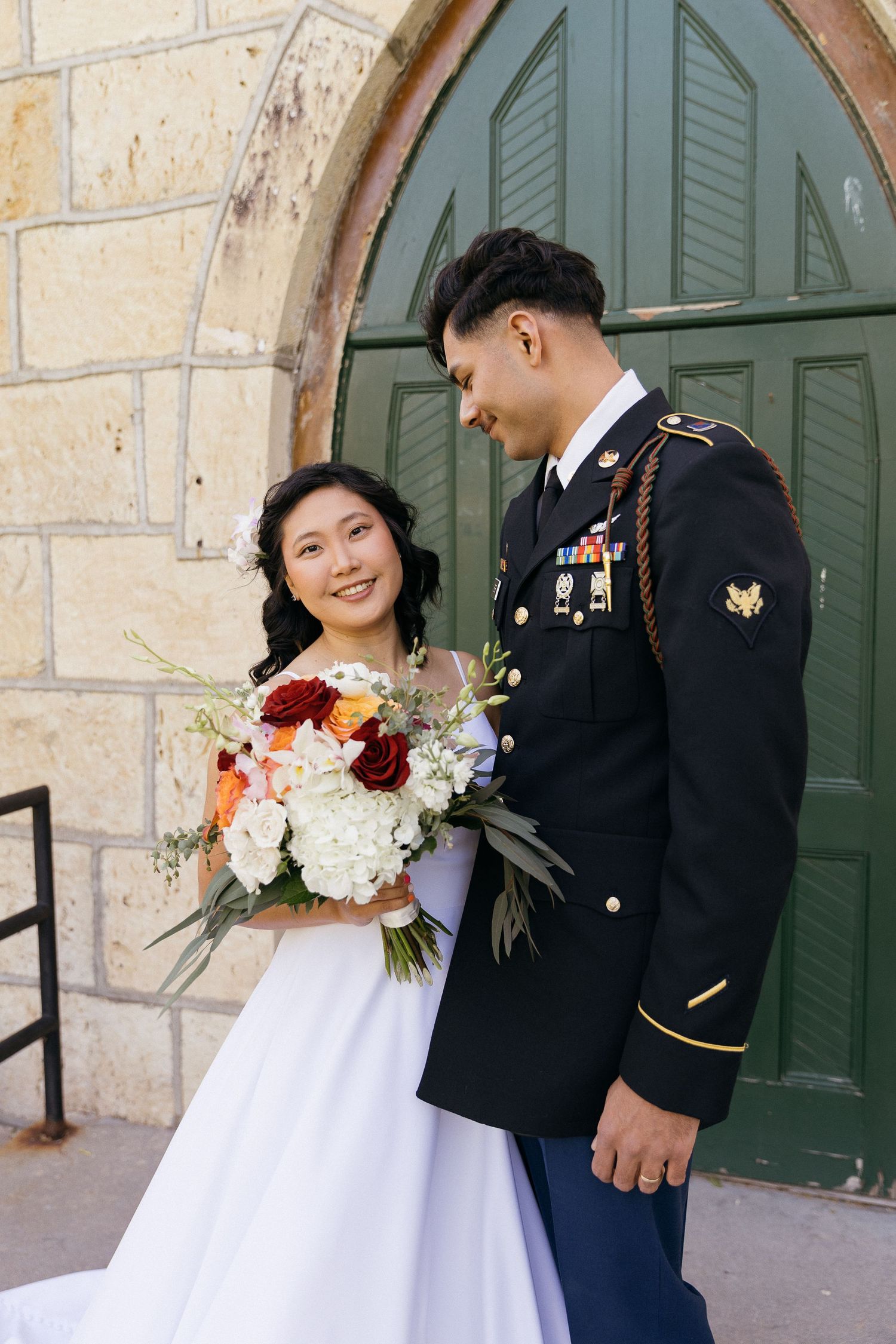 A romantic wedding portrait in front of a stone church with green doors.