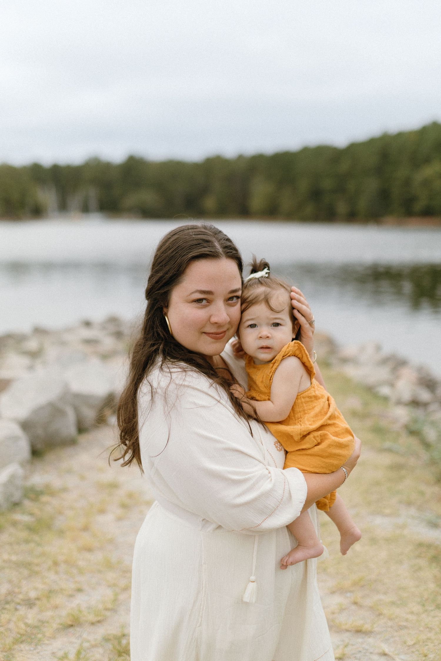 Parent and child in white and orange outfits pose together by peaceful lake.