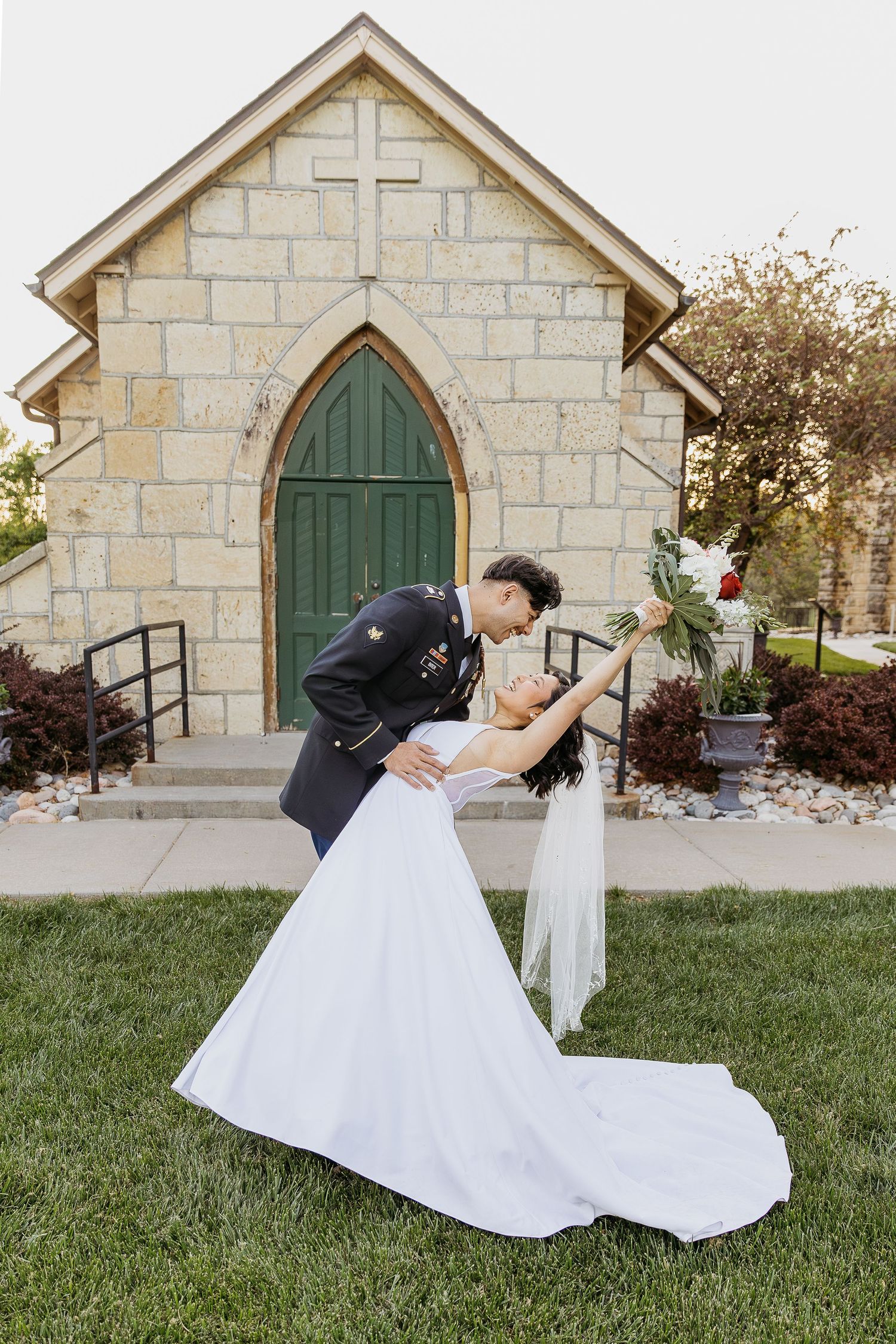 A romantic wedding photo in front of a stone chapel with a green arched door.