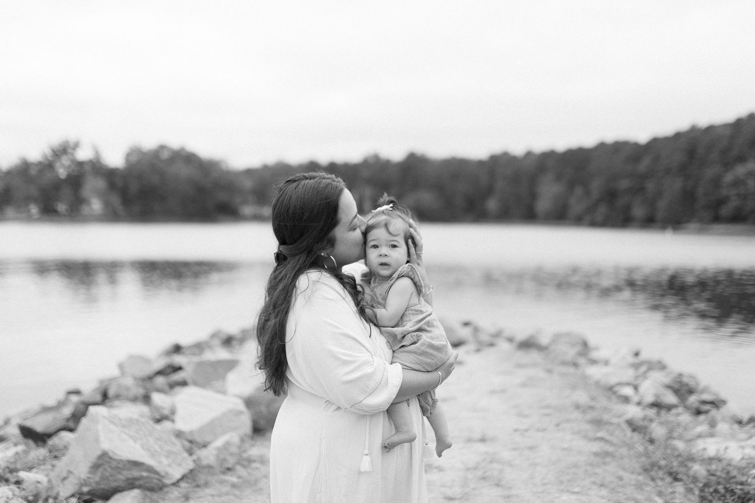 Black and white photo of mother and child sharing laughter on rocky shoreline.