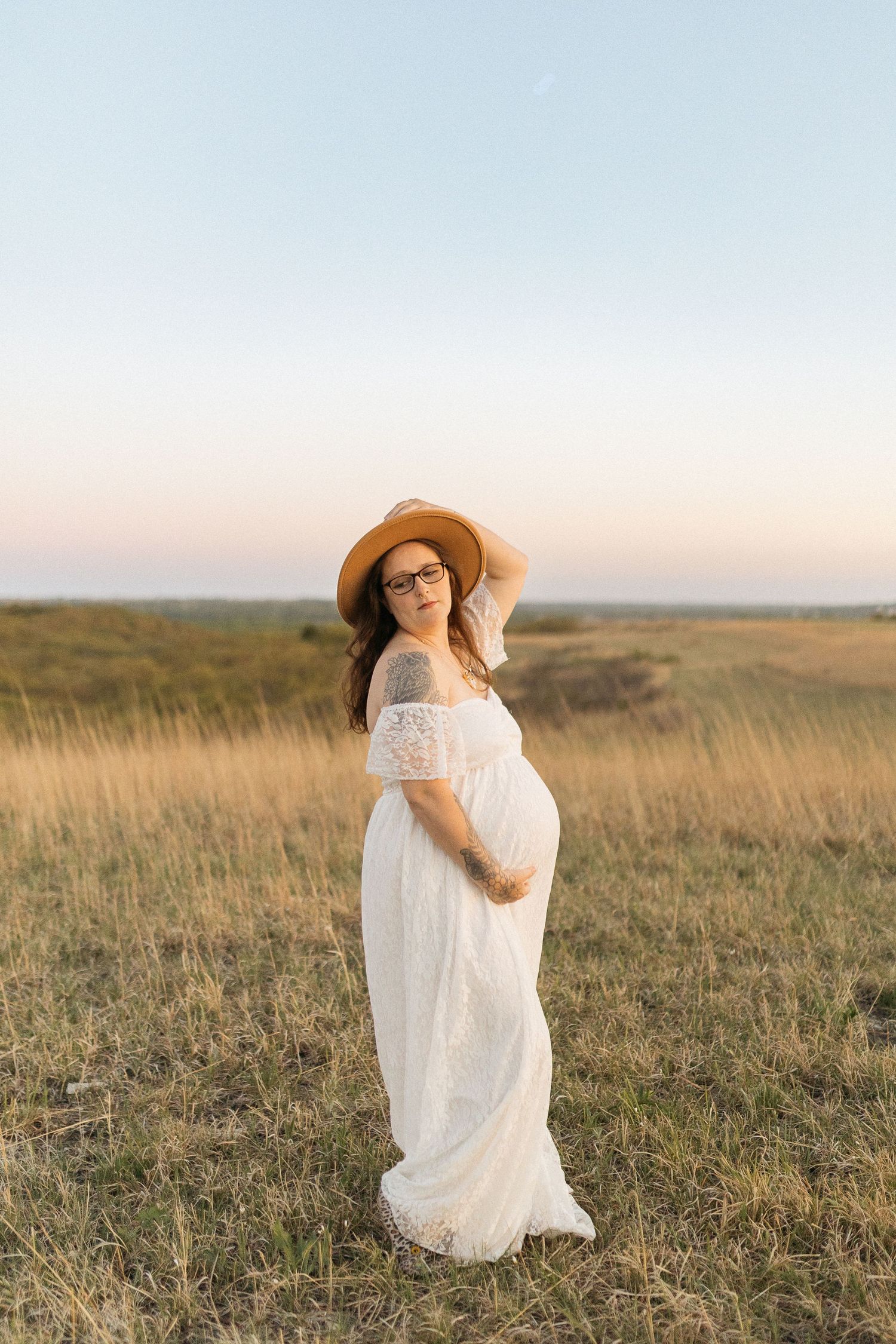 Ethereal maternity photo in white dress against golden hour prairie landscape.