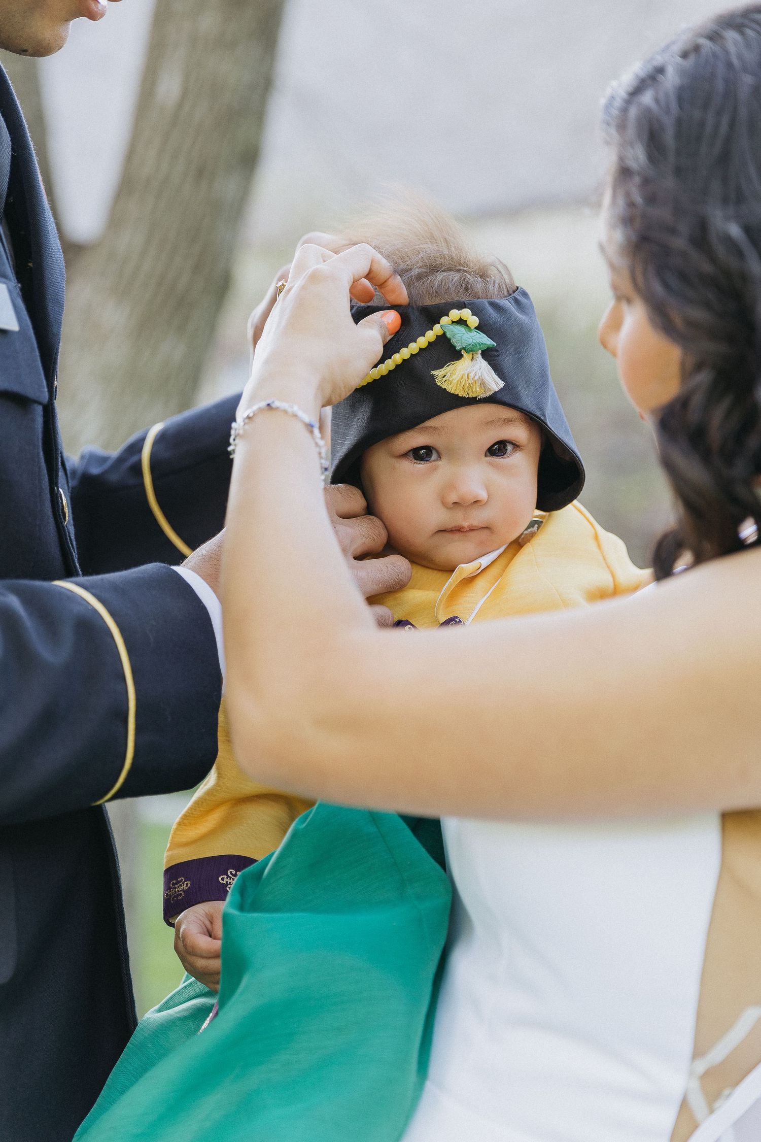 A small child in a yellow outfit gets help adjusting their hat during a formal event.
