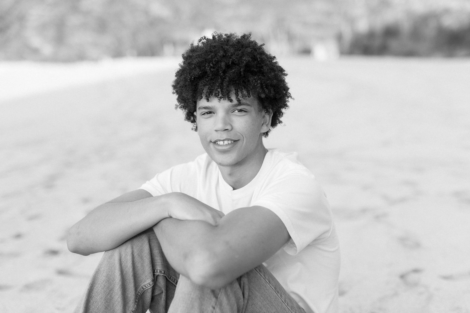 Black and white beach portrait showing relaxed smile while sitting on sand.waimea bay senior session north shore oahu hawaii