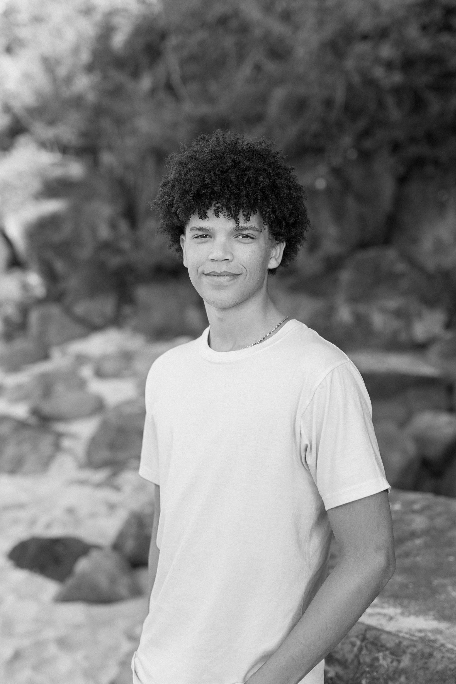 Black and white portrait of person in white t-shirt with natural rock background. waimea bay senior session north shore oahu hawaii