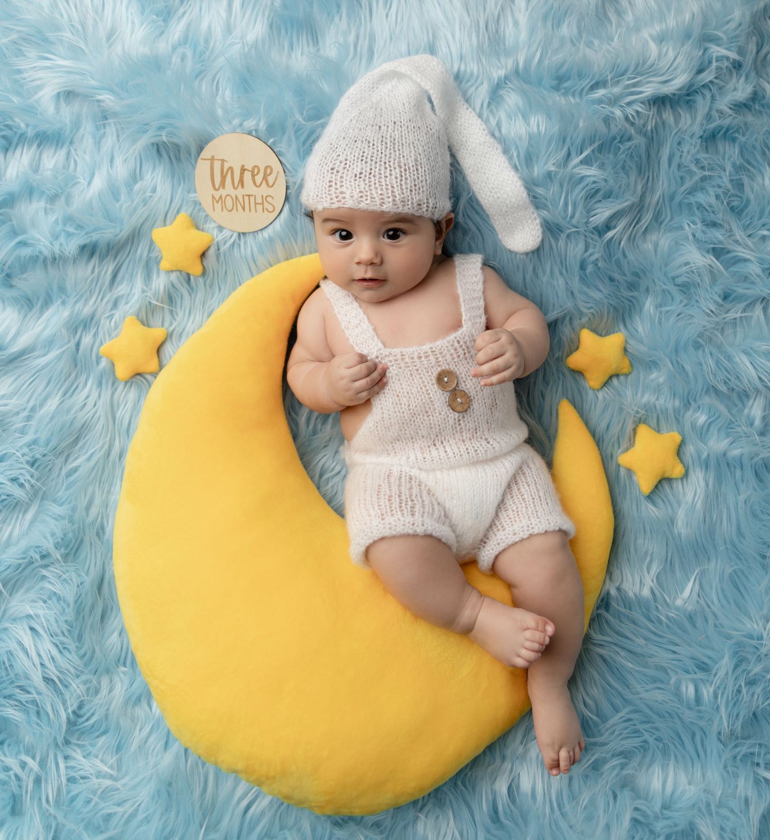 A baby boy sits on a moon prop, smiling during his milestone photo session.