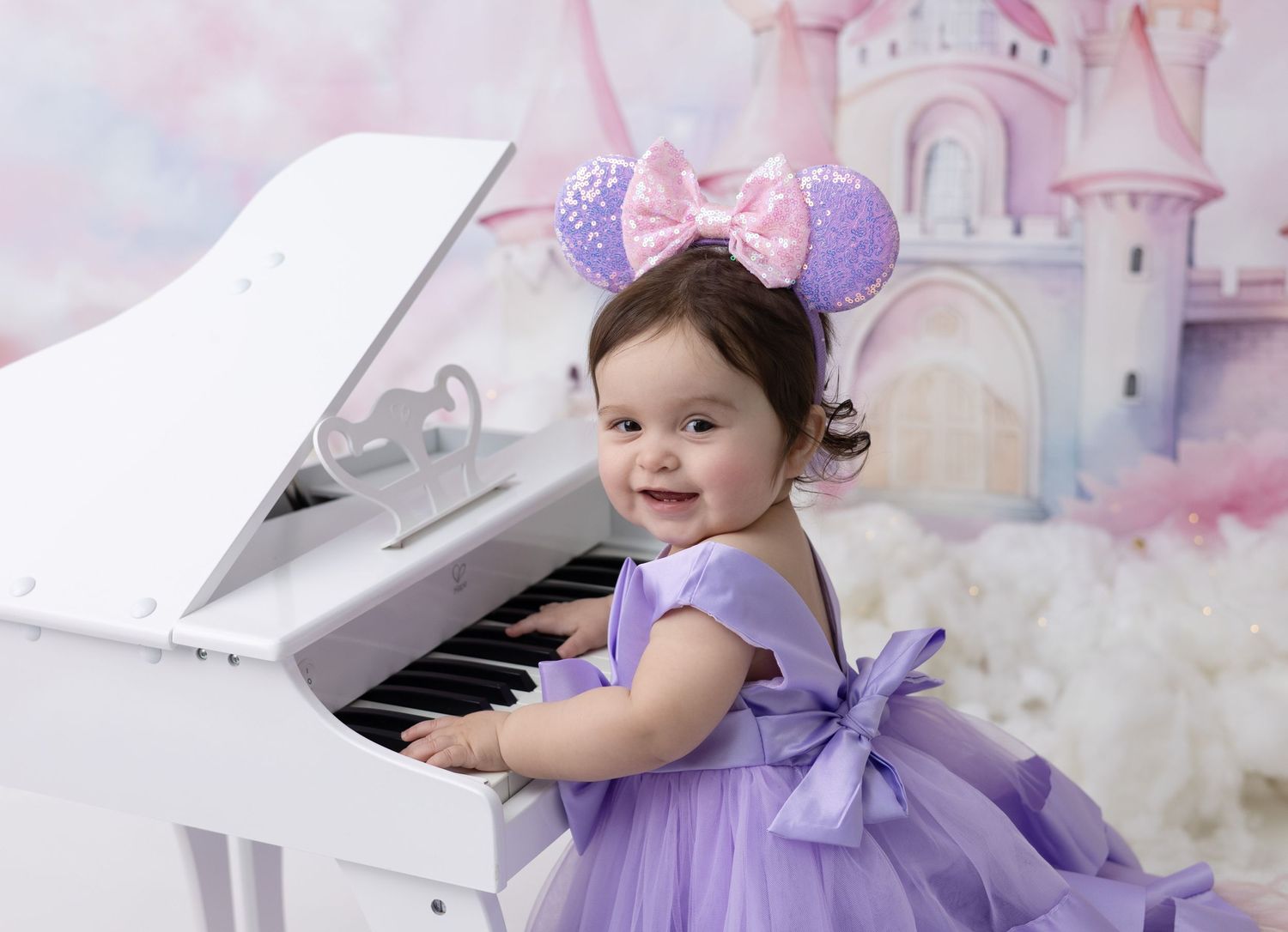 A one-year-old birthday girl in a Disney-themed outfit smiles surrounded by colorful decorations celebrating her magical first birthday