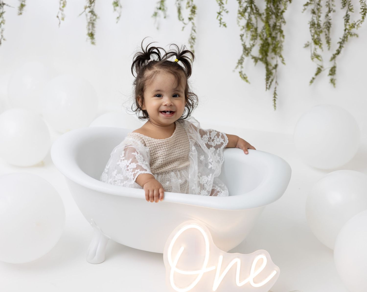 A one-year-old baby girl sits in a small, vintage-style clawfoot bathtub, splashing and smiling with pure joy.
