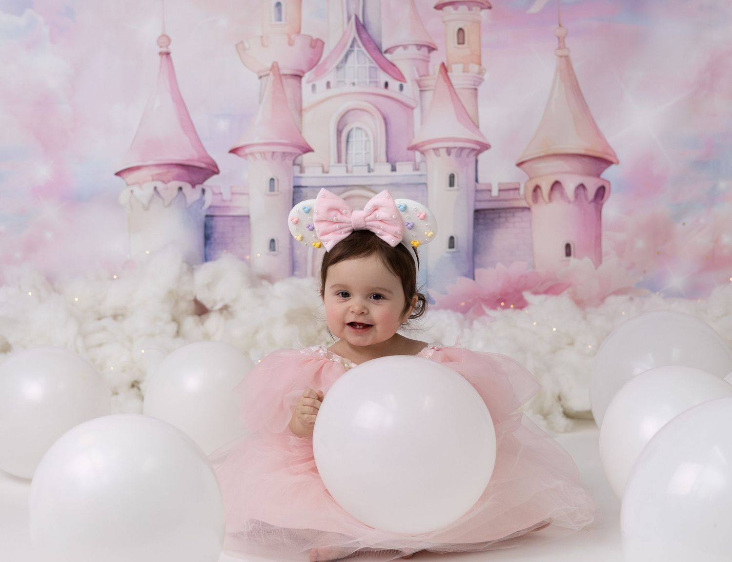 A one-year-old birthday girl in a Disney-themed outfit smiles surrounded by colorful decorations celebrating her magical first birthday