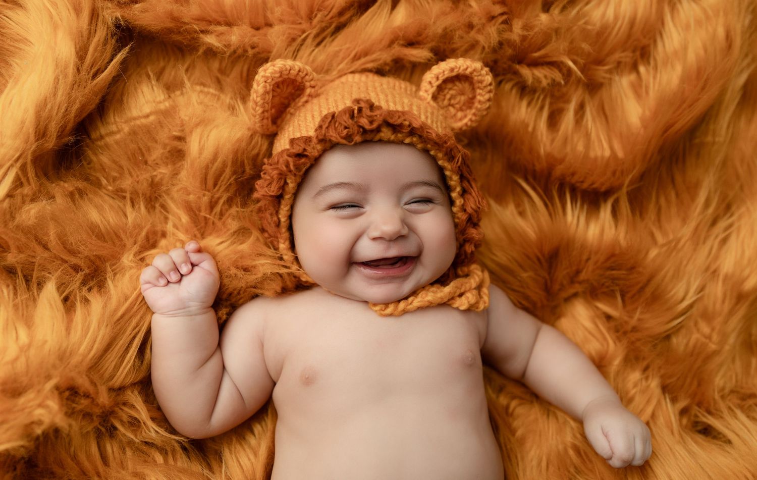 A baby boy smiles adorably in a lion-themed outfit during his milestone session.