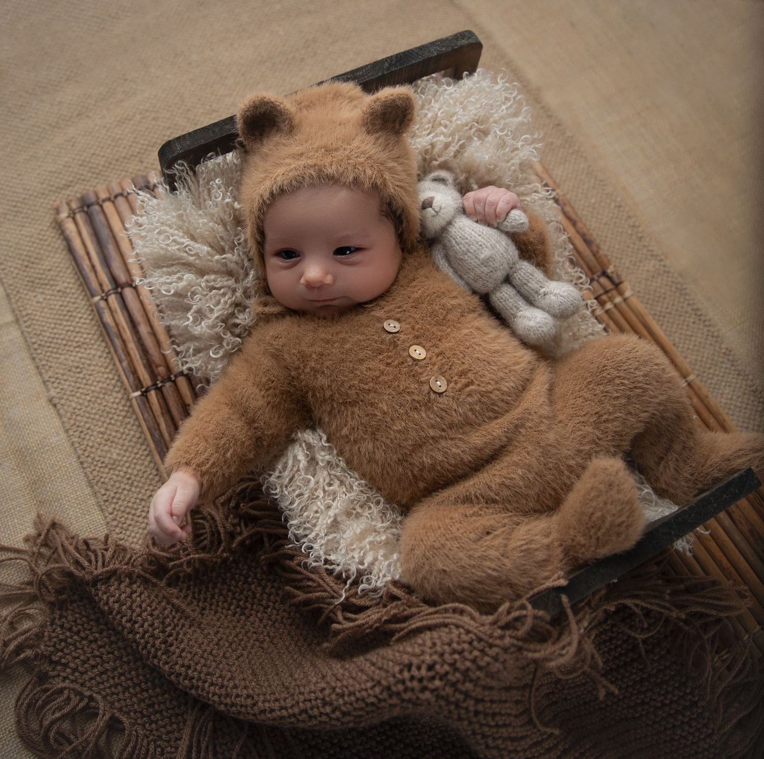 A baby boy in a cute baby bear outfit lays on a cozy bed during his milestone session, surrounded by soft blankets.
