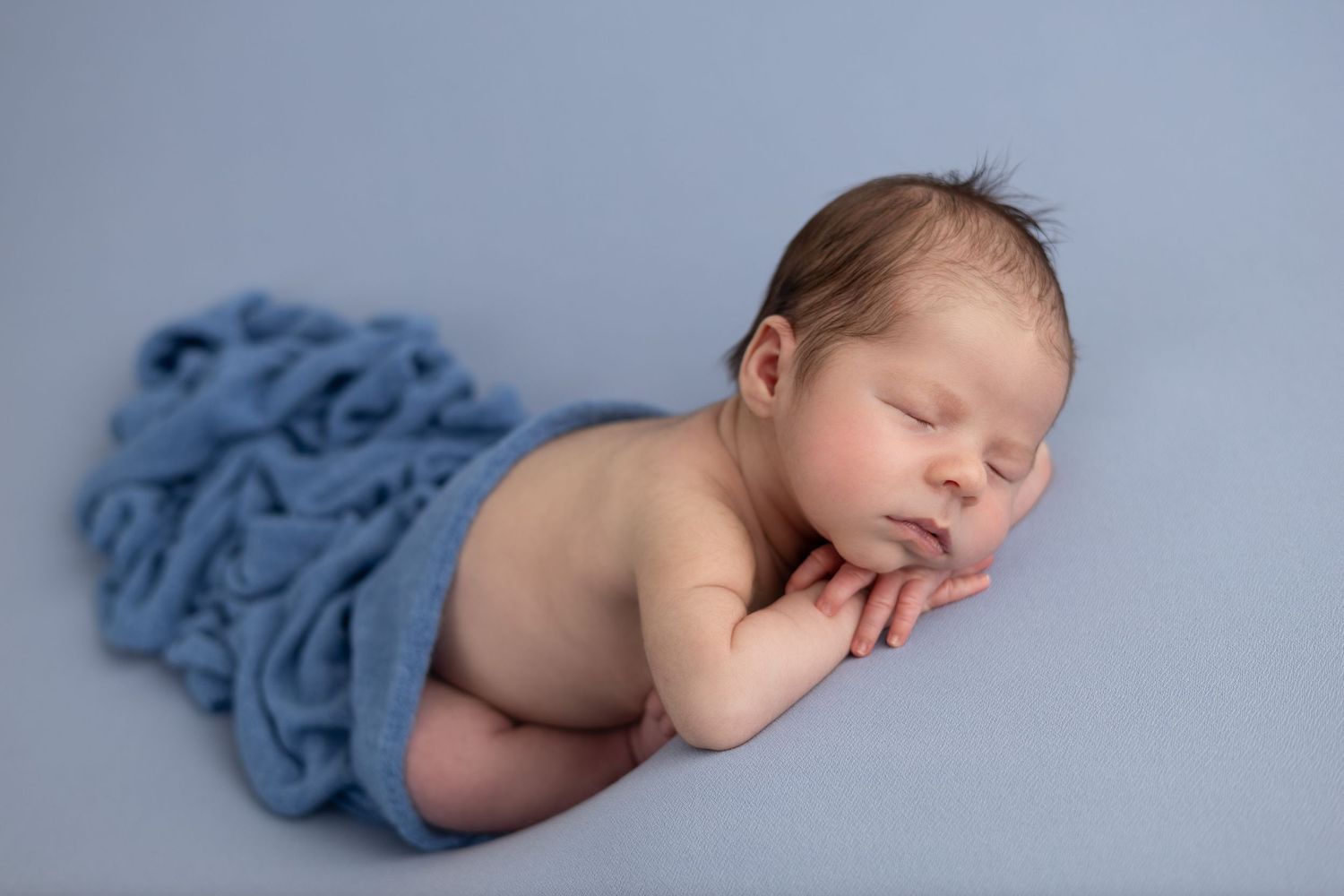 A newborn baby boy sleeps peacefully with his chin resting on his hand, in a soft and serene pose.
