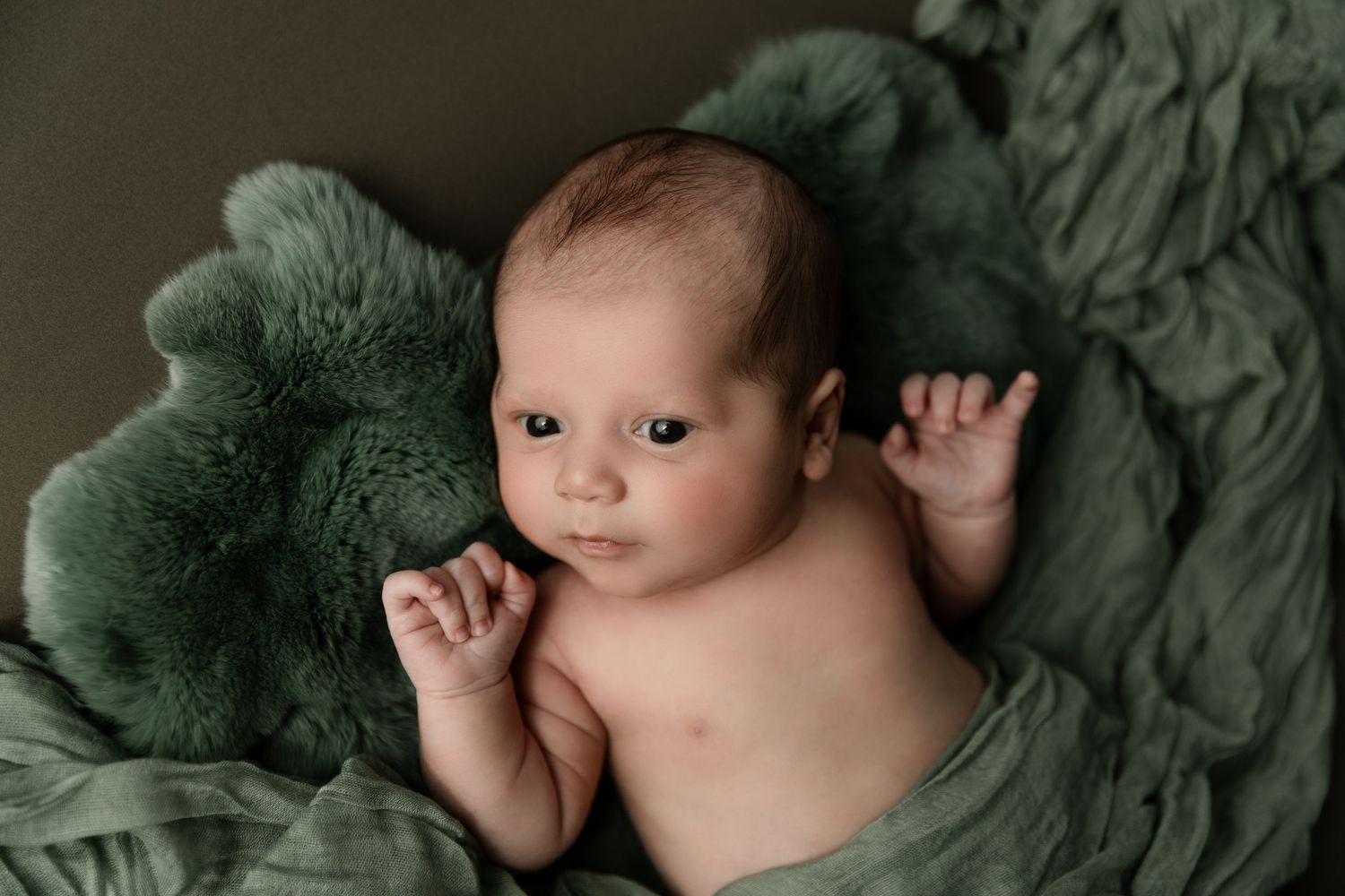 A newborn baby boy is posed on his back with eyes wide open during his in-home newborn session in Orange County, CA.