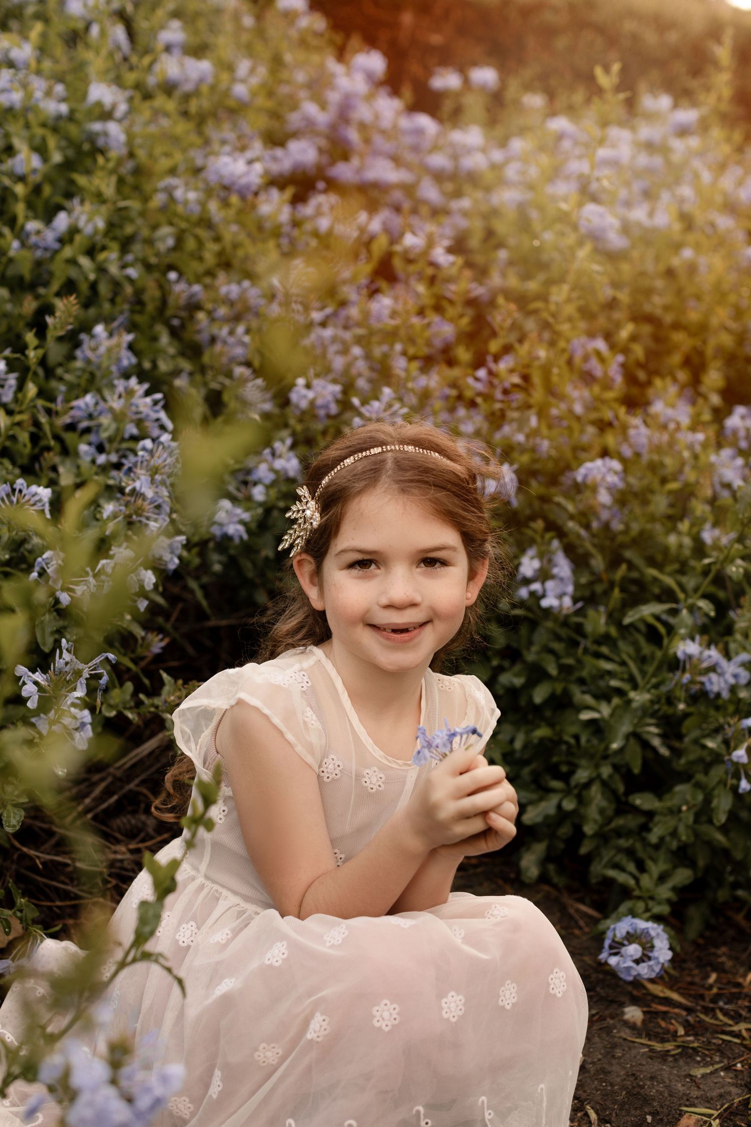 A little girl is surrounded by flowers during her family outdoor session in Orange County, CA, creating a sweet and whimsical moment.