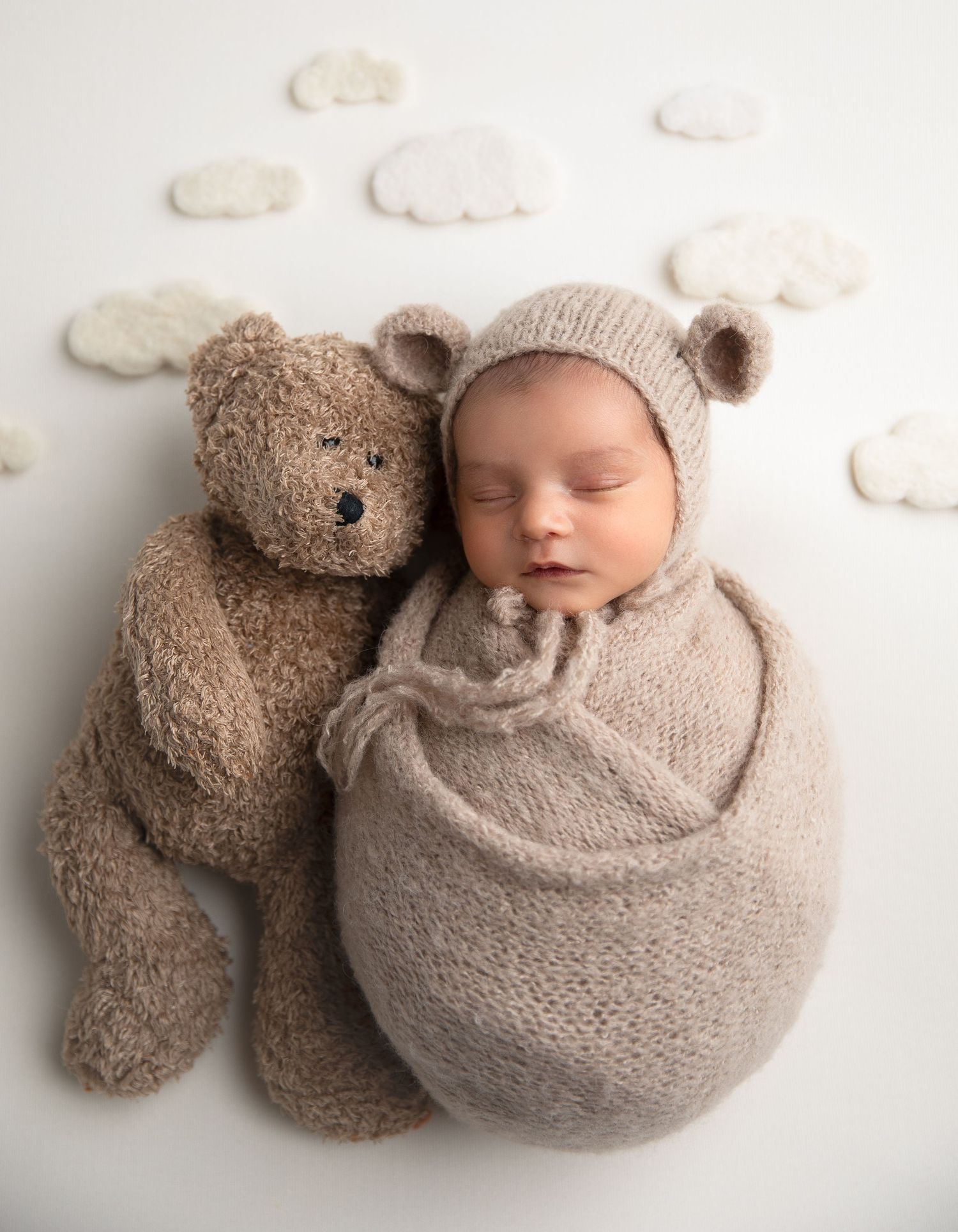 A swaddled newborn baby boy sleeps peacefully next to a teddy bear.