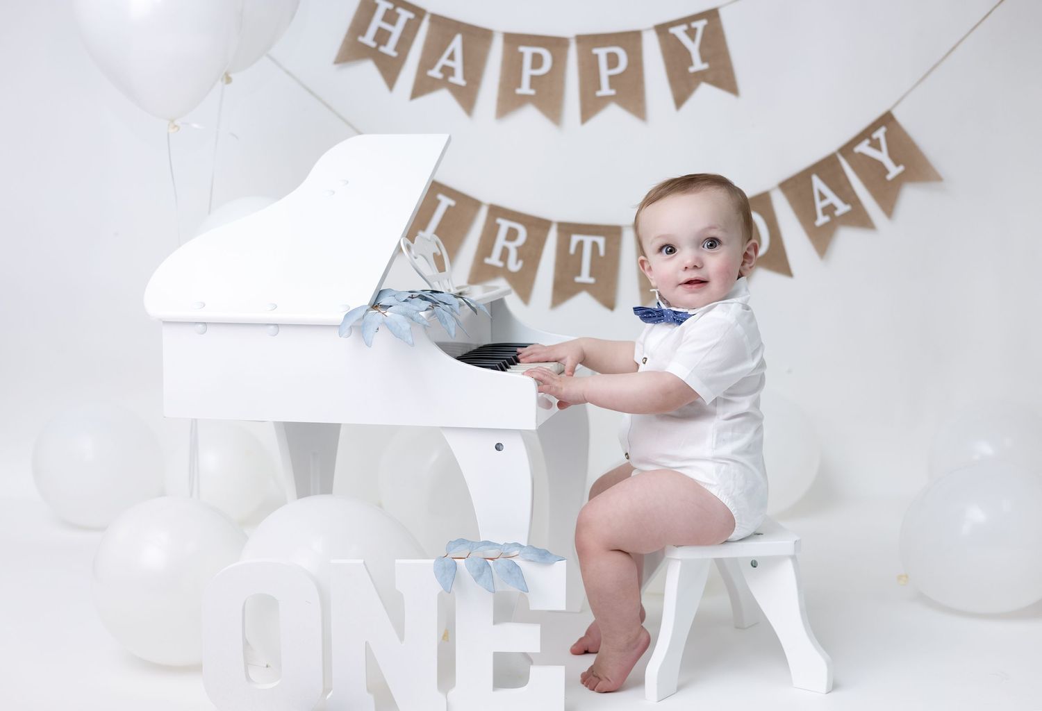 A birthday boy plays a piano in an all-white themed setup, creating a timeless and elegant first birthday moment.