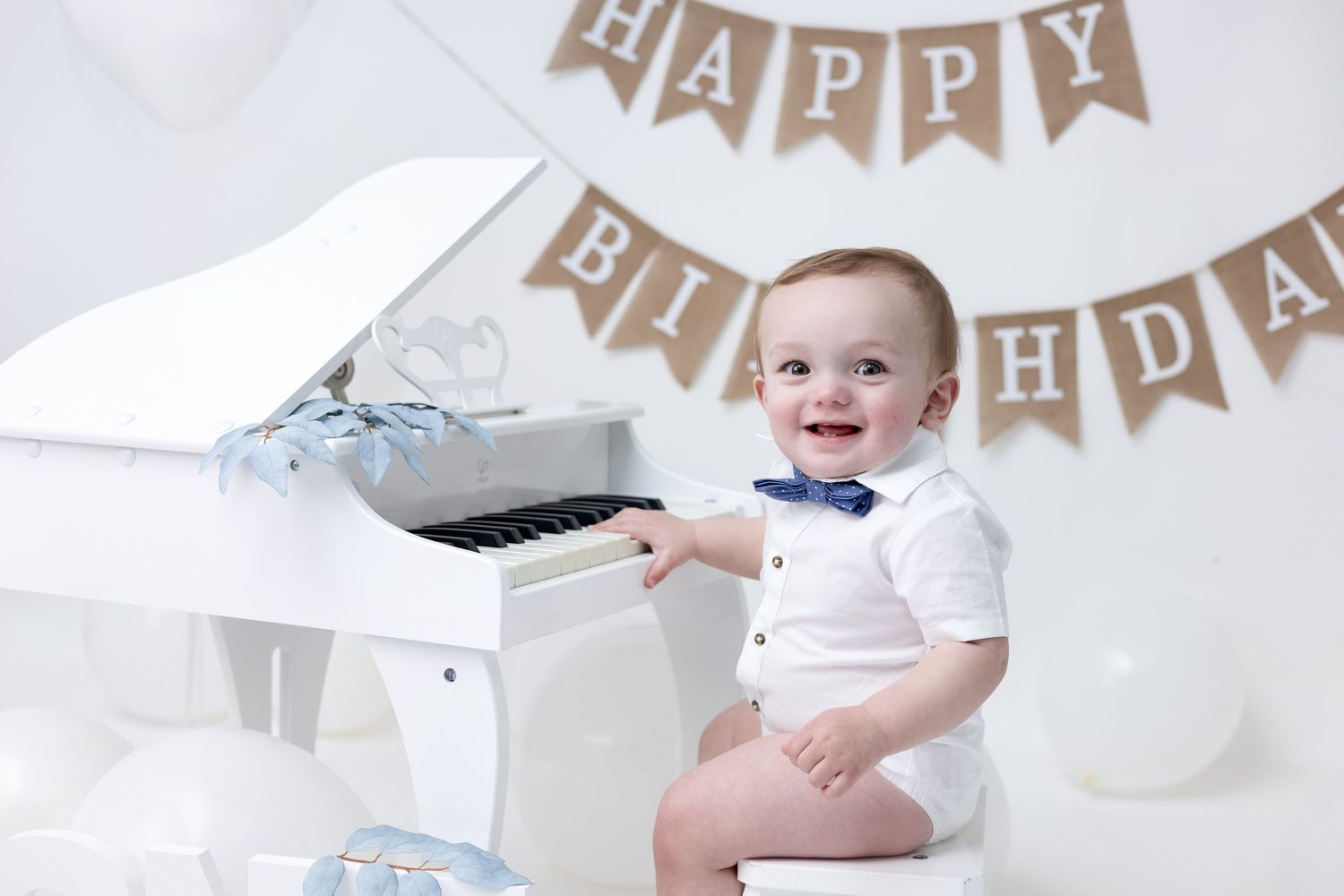 A birthday boy plays a piano in an all-white themed setup, creating a timeless and elegant first birthday moment.