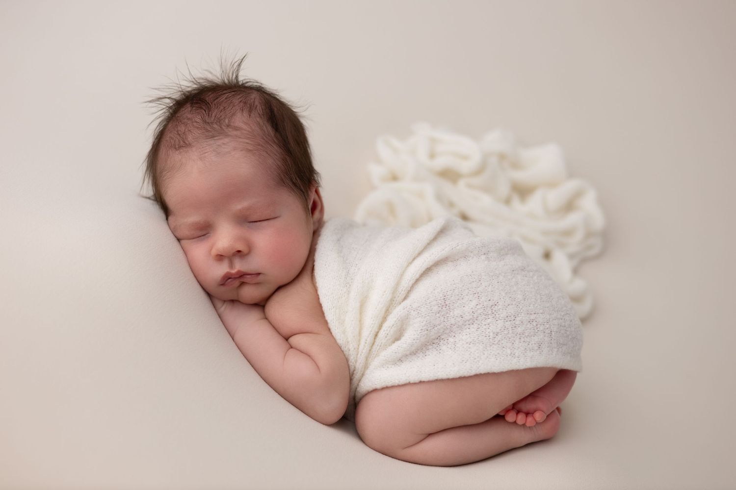 A newborn baby boy is peacefully posed in the bum-up position, resting on a soft, textured blanket