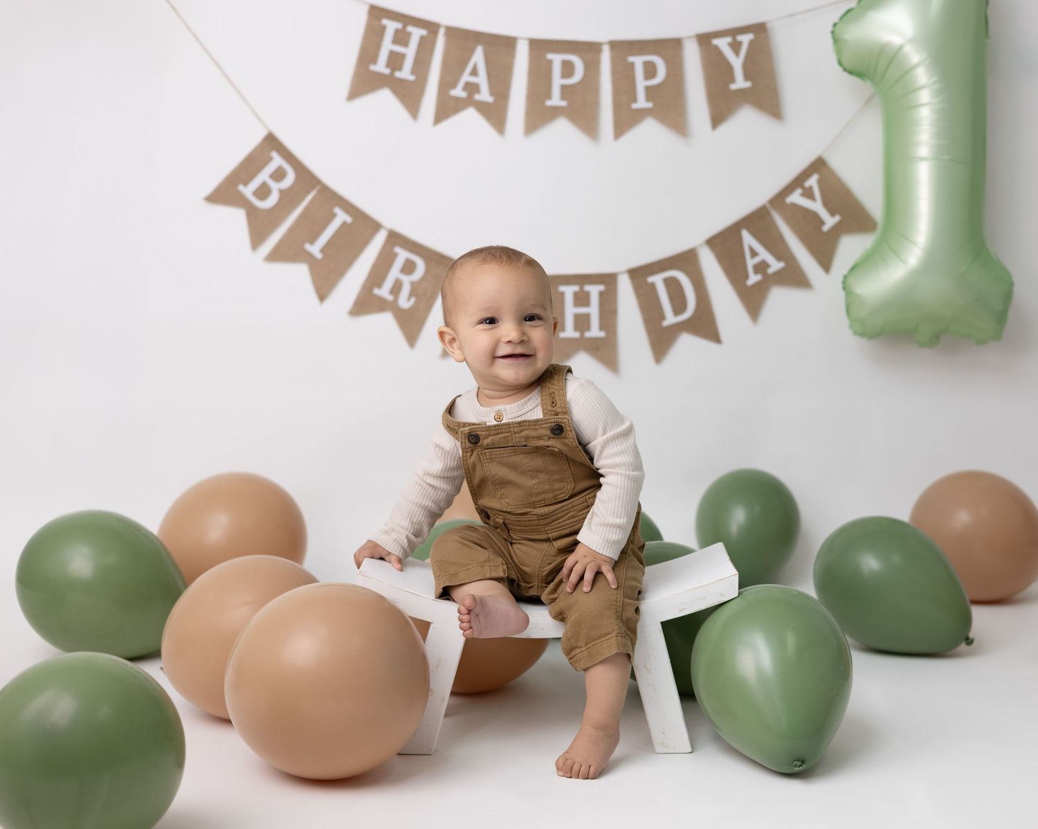 A one-year-old baby sits in a neutral-themed first birthday setup, featuring soft, earthy tones for a timeless and elegant look.