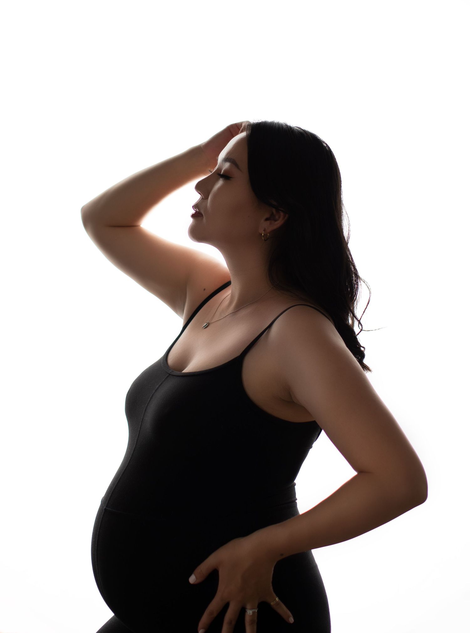 A silhouette of a pregnant woman in the studio, showcasing the beauty of her baby bump against soft, dramatic lighting.