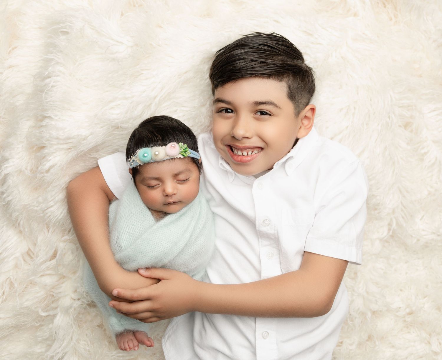 A newborn baby girl is gently posed with her brother during an in-home photography session, capturing a sweet sibling moment.