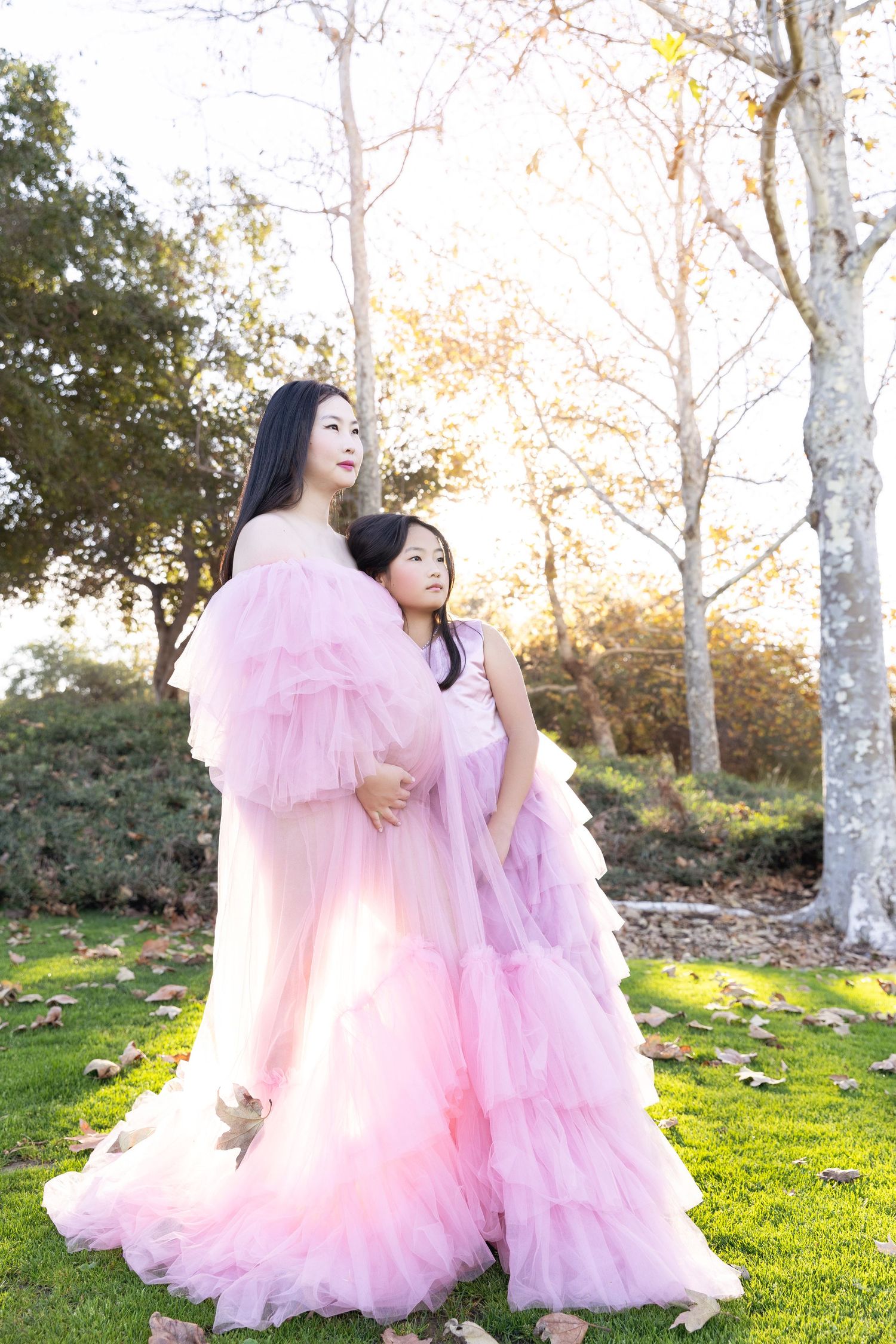 A mother poses with her daughter during an outdoor maternity photoshoot, capturing a tender and joyful moment.