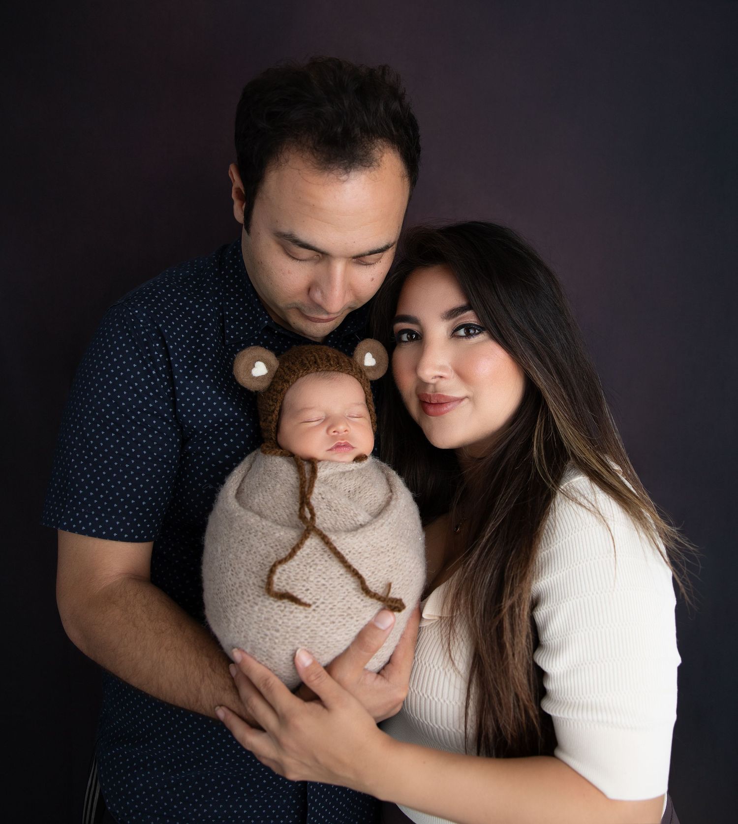 A newborn baby boy is gently posed with his parents, capturing a tender family moment.